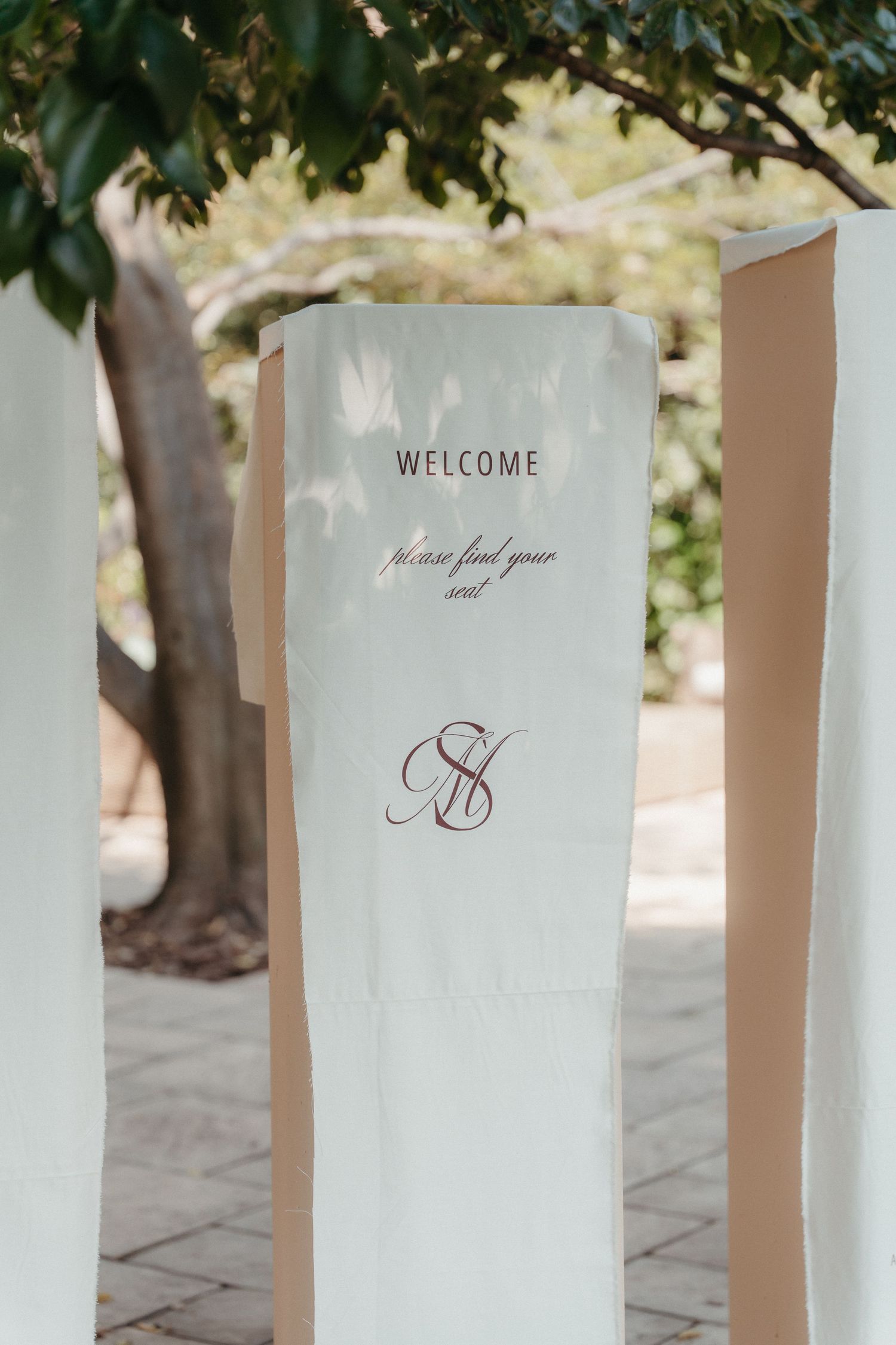 Elegant wedding welcome sign with monogram and 'please find your seat' message displayed outdoors.