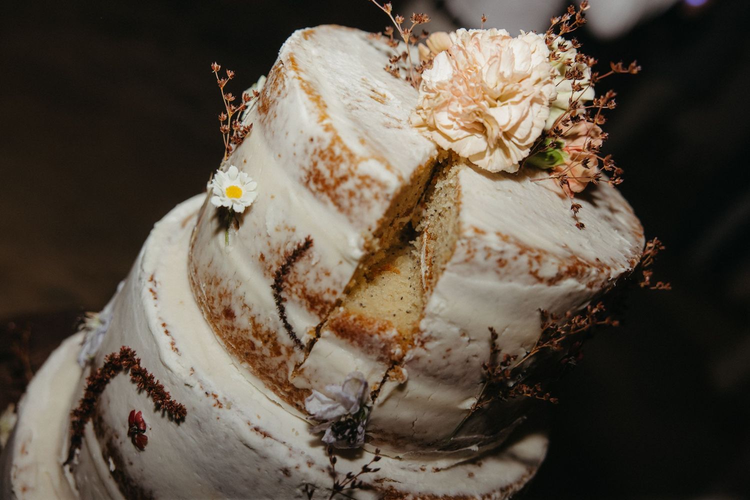 Rustic naked wedding cake with white frosting, floral decorations, and a slice cut out revealing golden sponge layers.