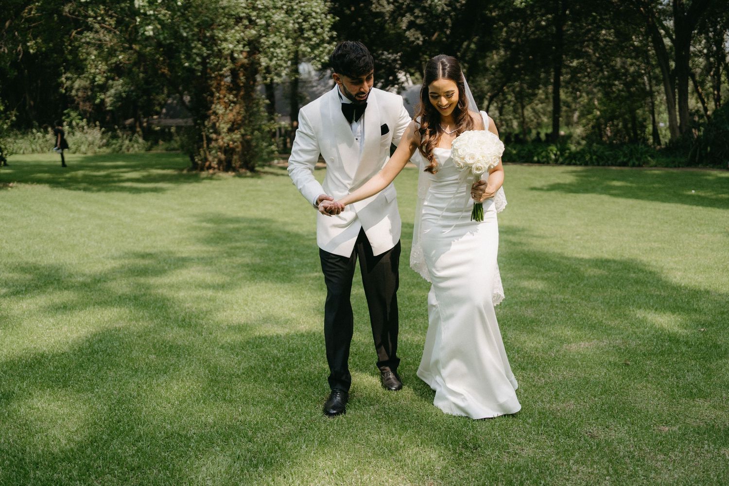 A couple walking together on a lush green lawn at an outdoor wedding celebration.