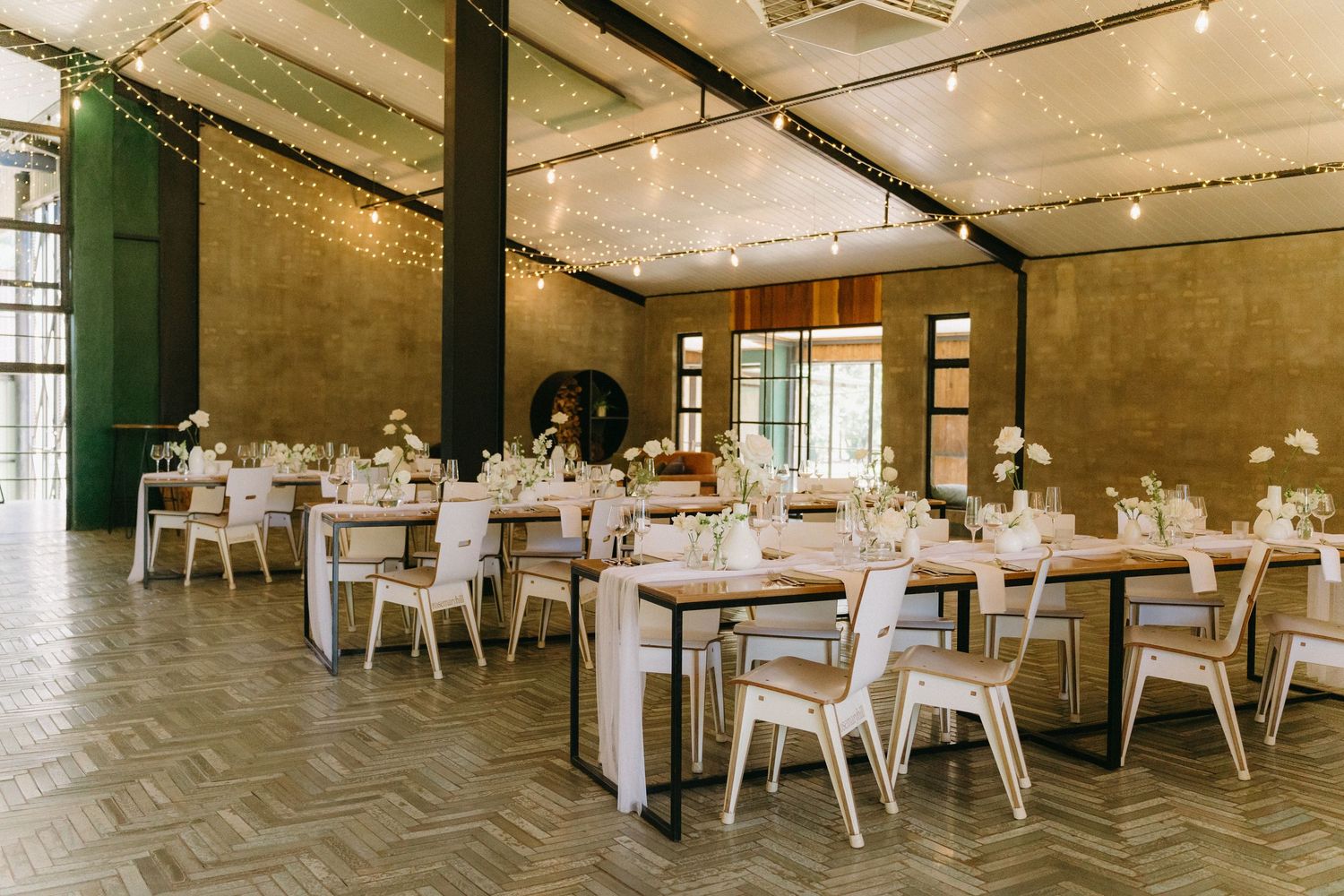 Modern event space with white dining tables and chairs set up for a wedding reception in an industrial-style room.