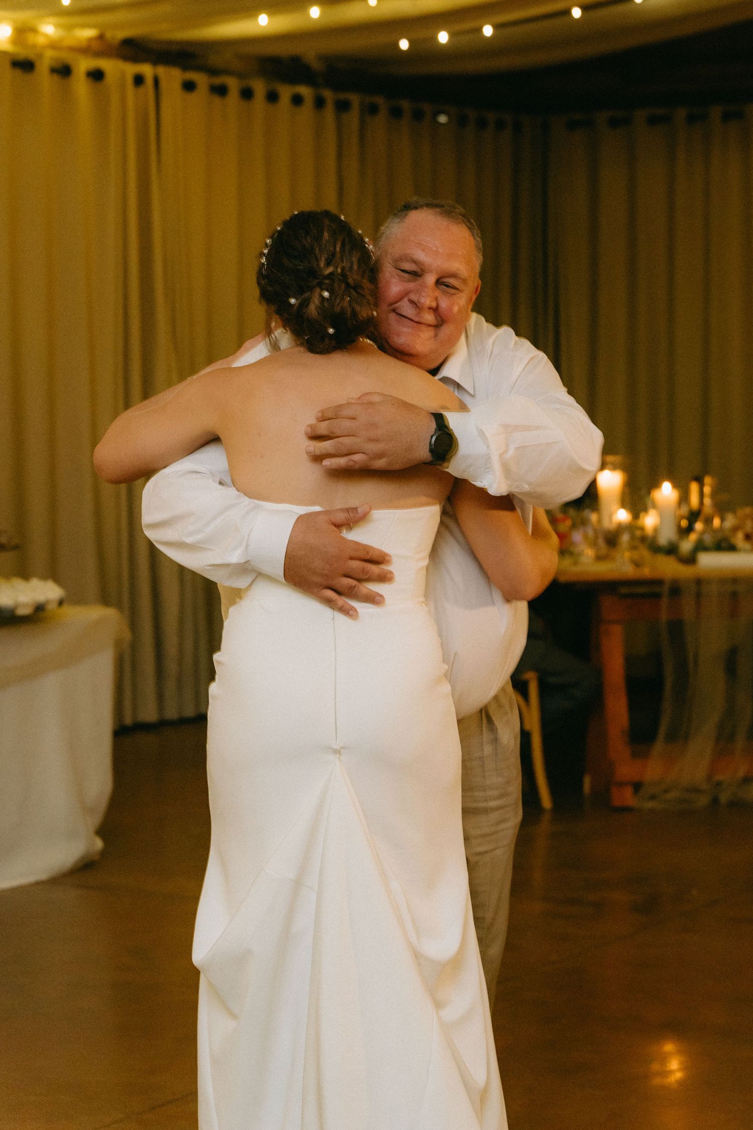 Wedding guests share emotional embraces during a reception in a warmly lit venue.