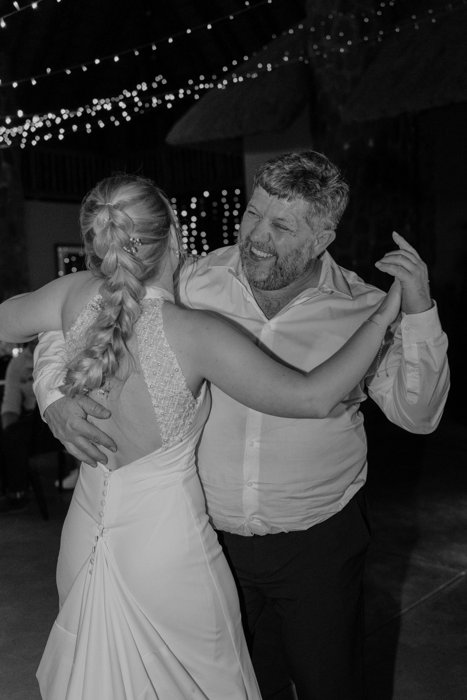 Black and white photo of a couple dancing at their wedding reception under string lights.