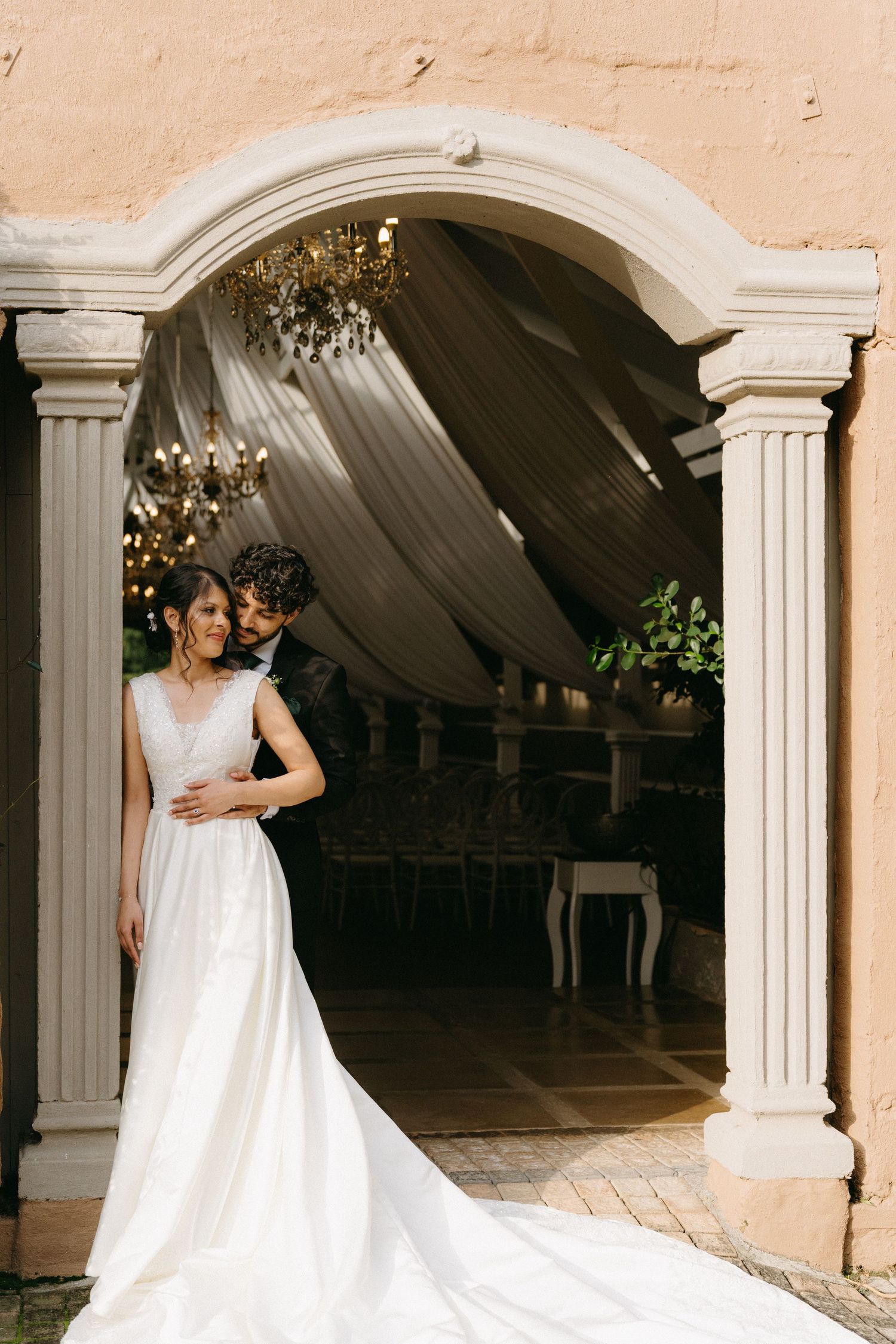 Elegant wedding couple posing in an archway with draped fabric and chandeliers.