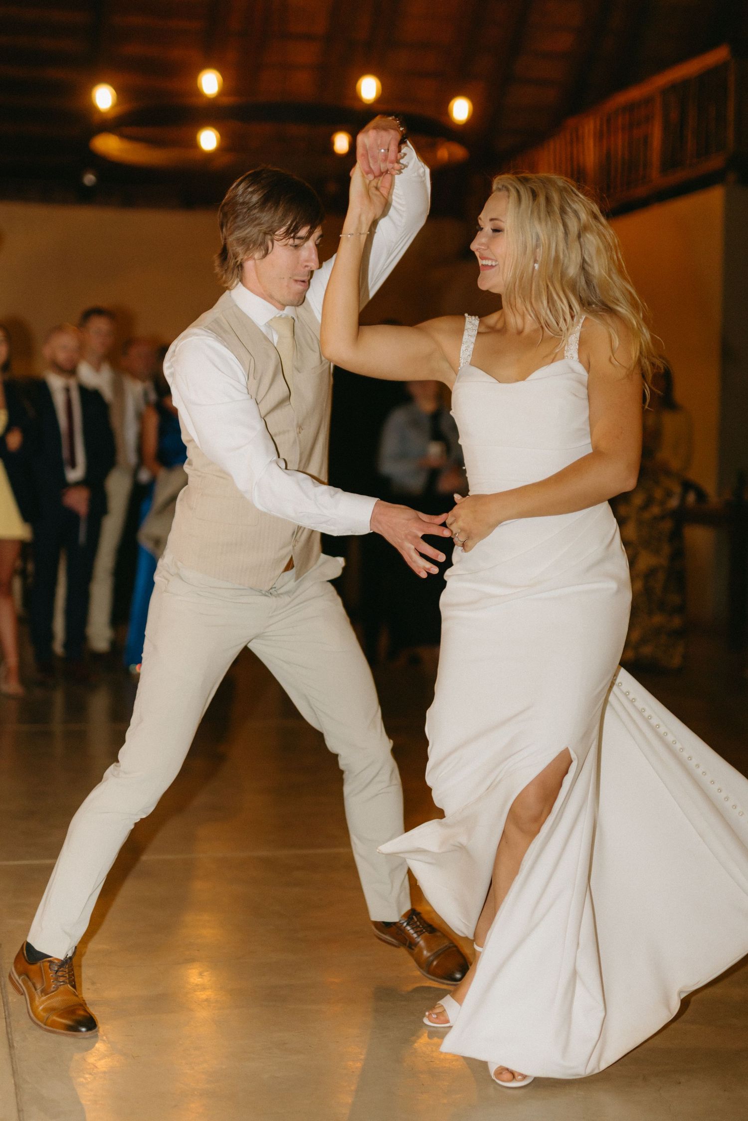 Wedding couple dancing energetically on a wooden floor under warm venue lighting.