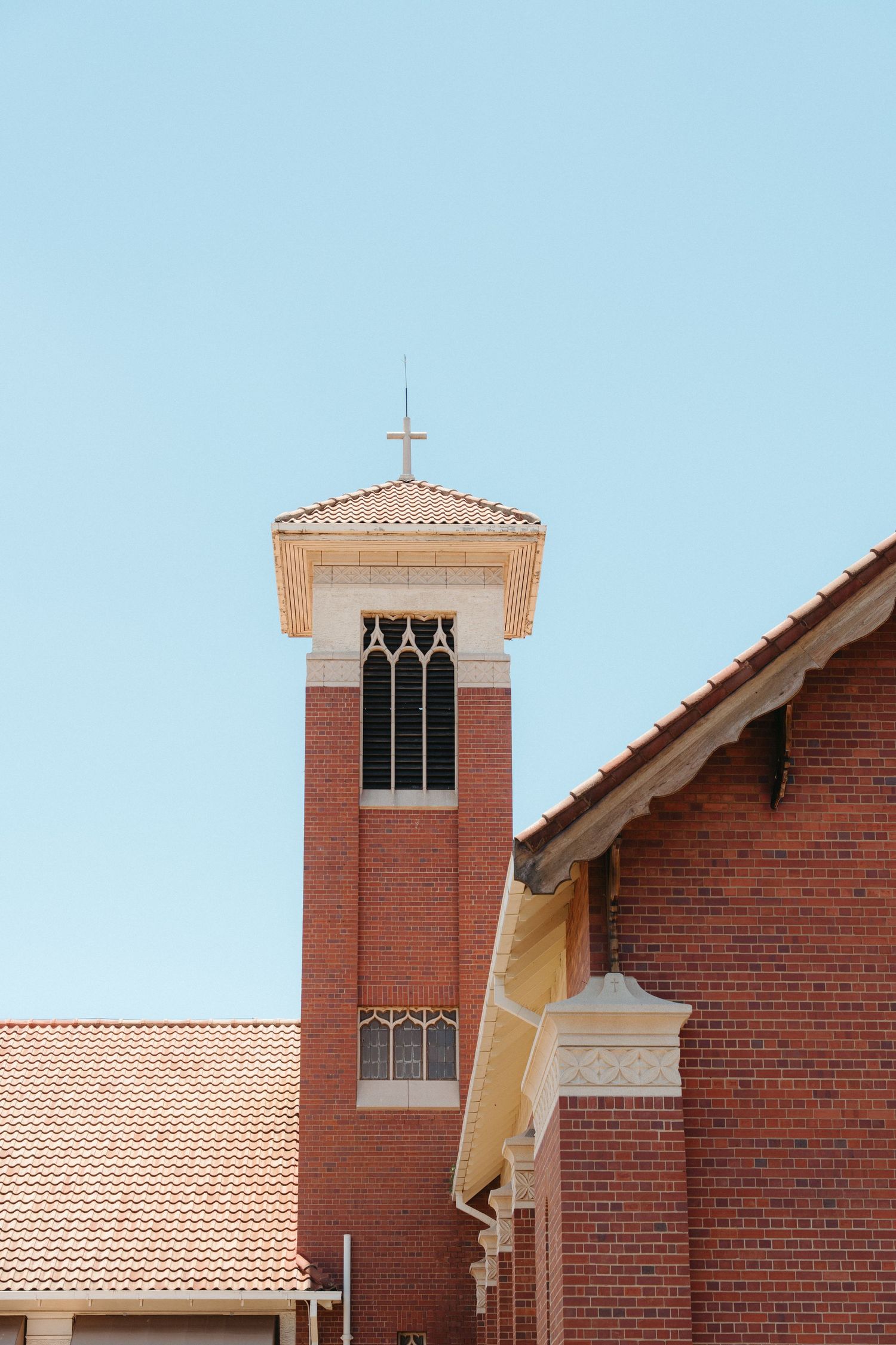 A brick church building with a tall bell tower and terracotta roof tiles against a blue sky.