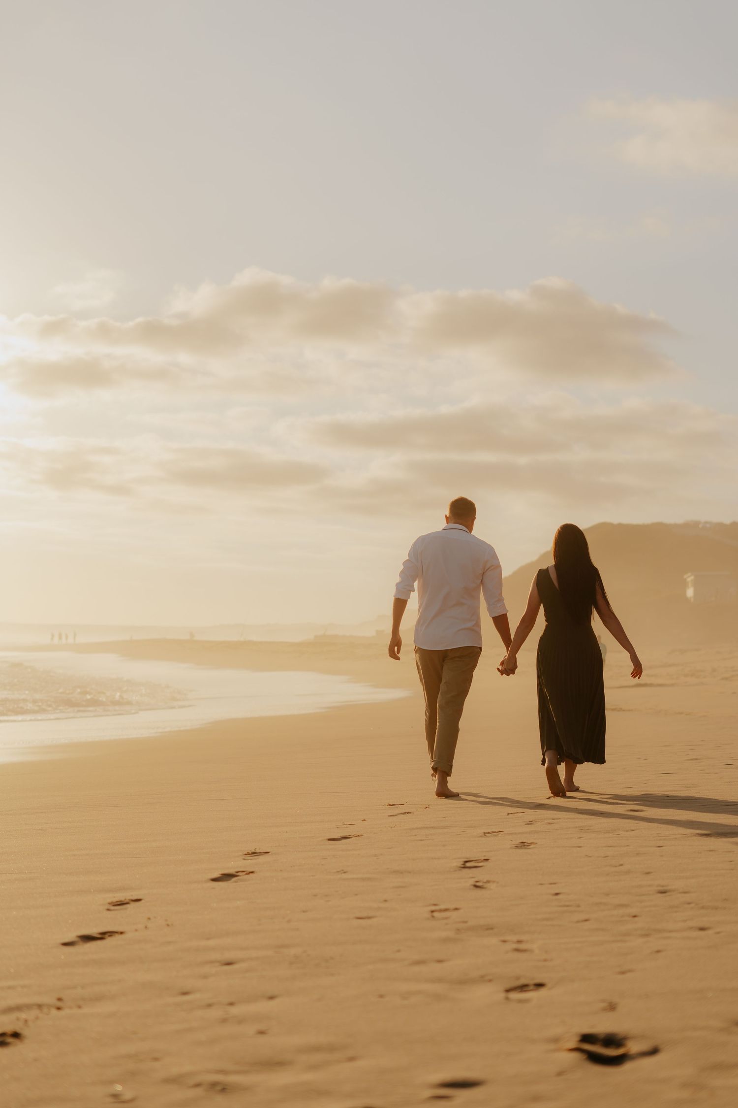 A couple walks hand in hand on a sandy beach in the Western Cape at sunset leaving footprints in their wake.