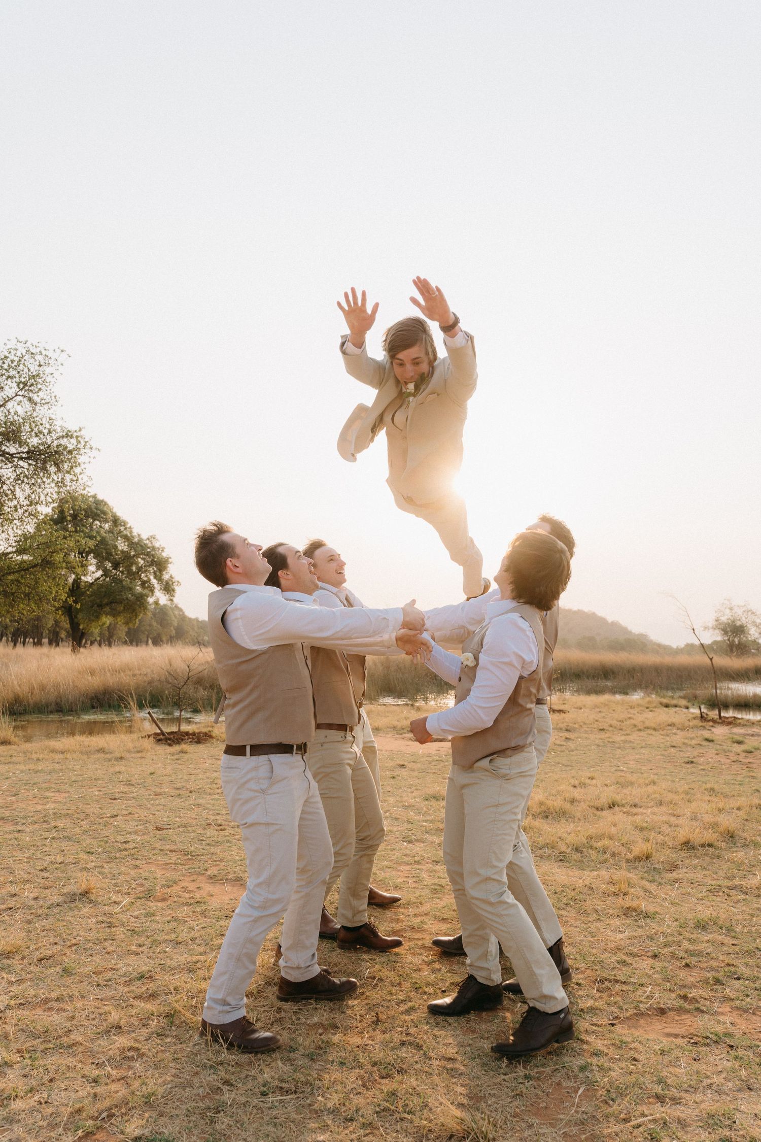Playful couple in light colored outfits dancing and twirling together in a golden field at sunset.
