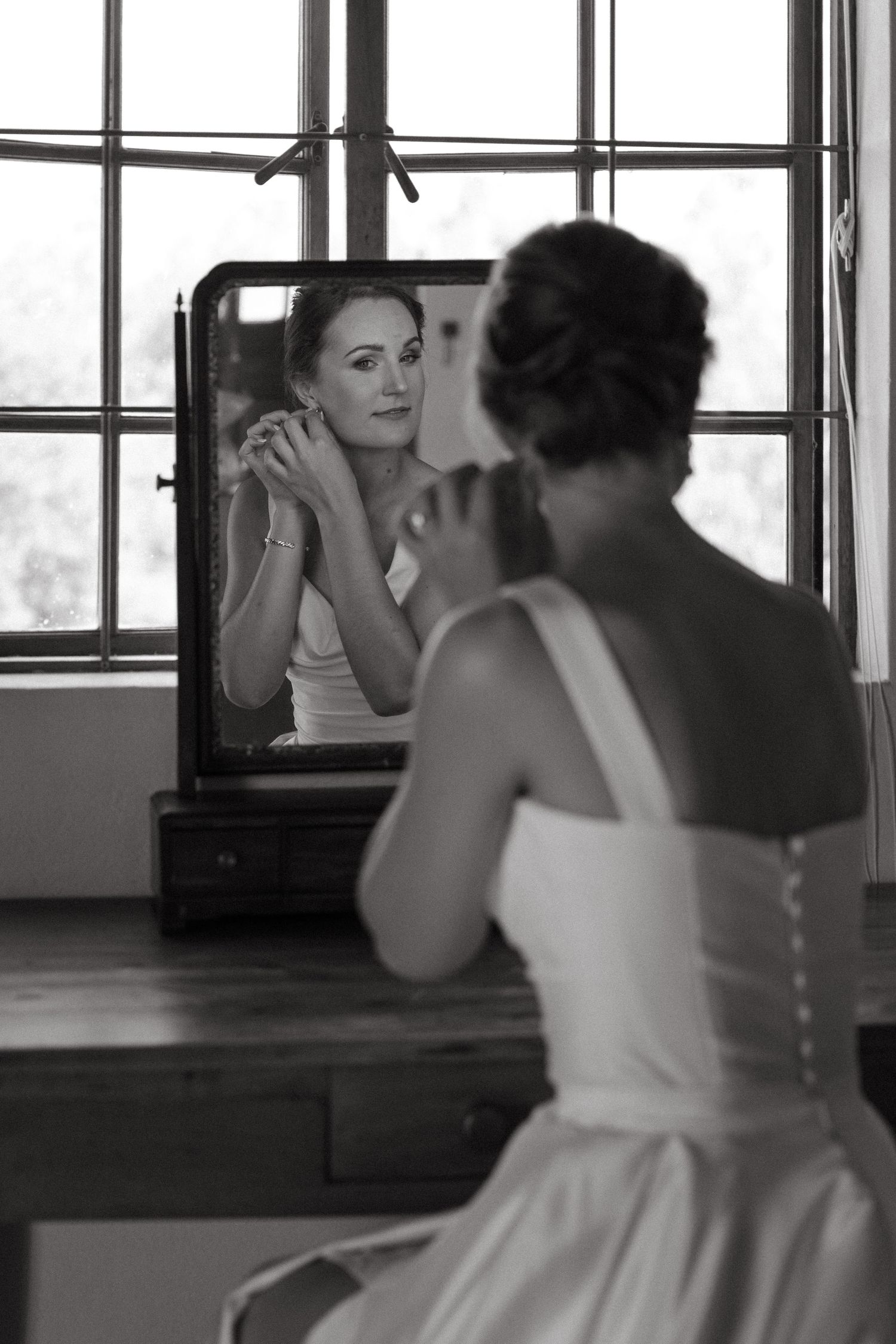A person in a white dress practices dance moves in front of a mirrored studio wall.