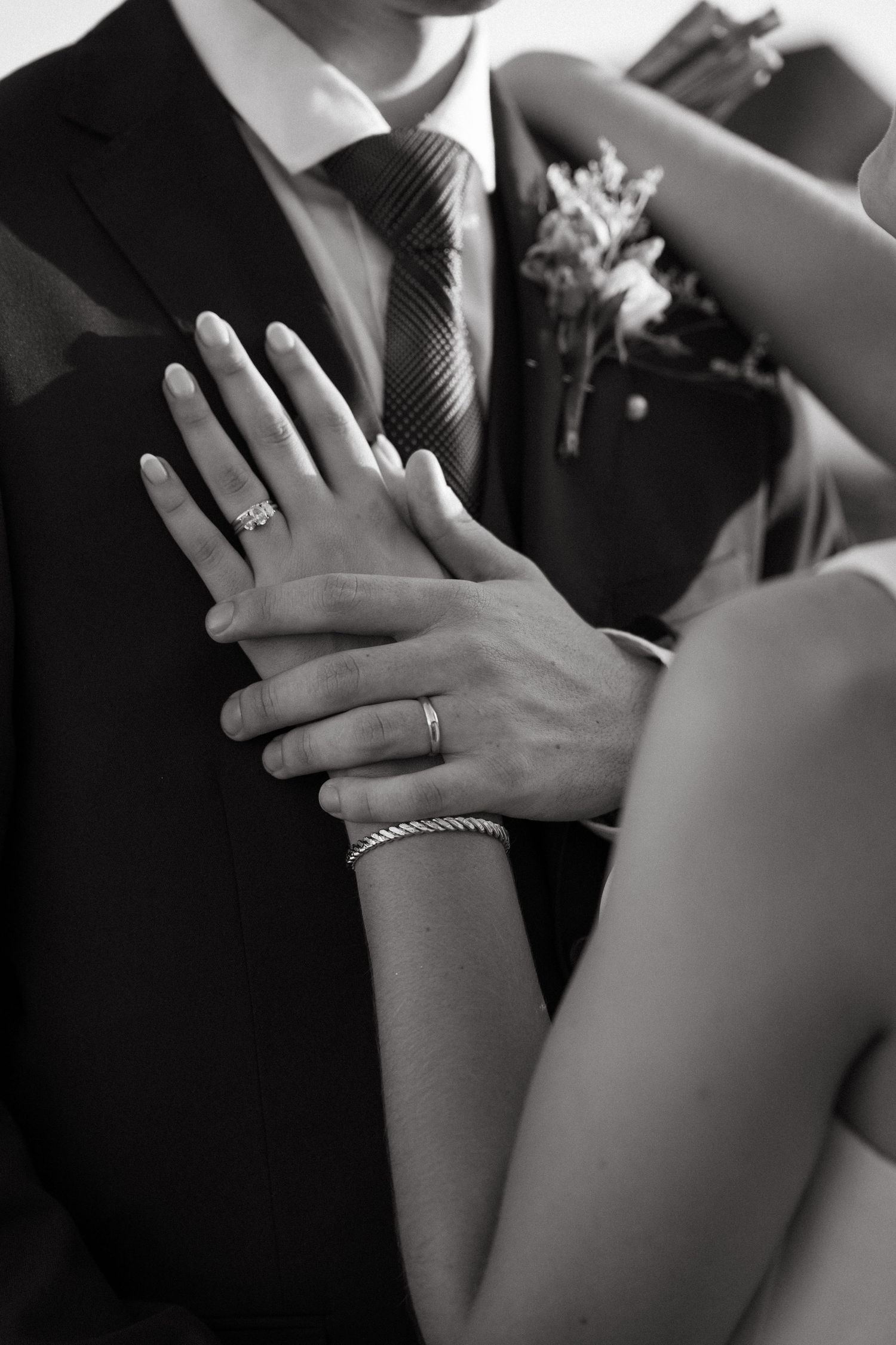 Black and white close-up of hands with wedding rings in an intimate moment.