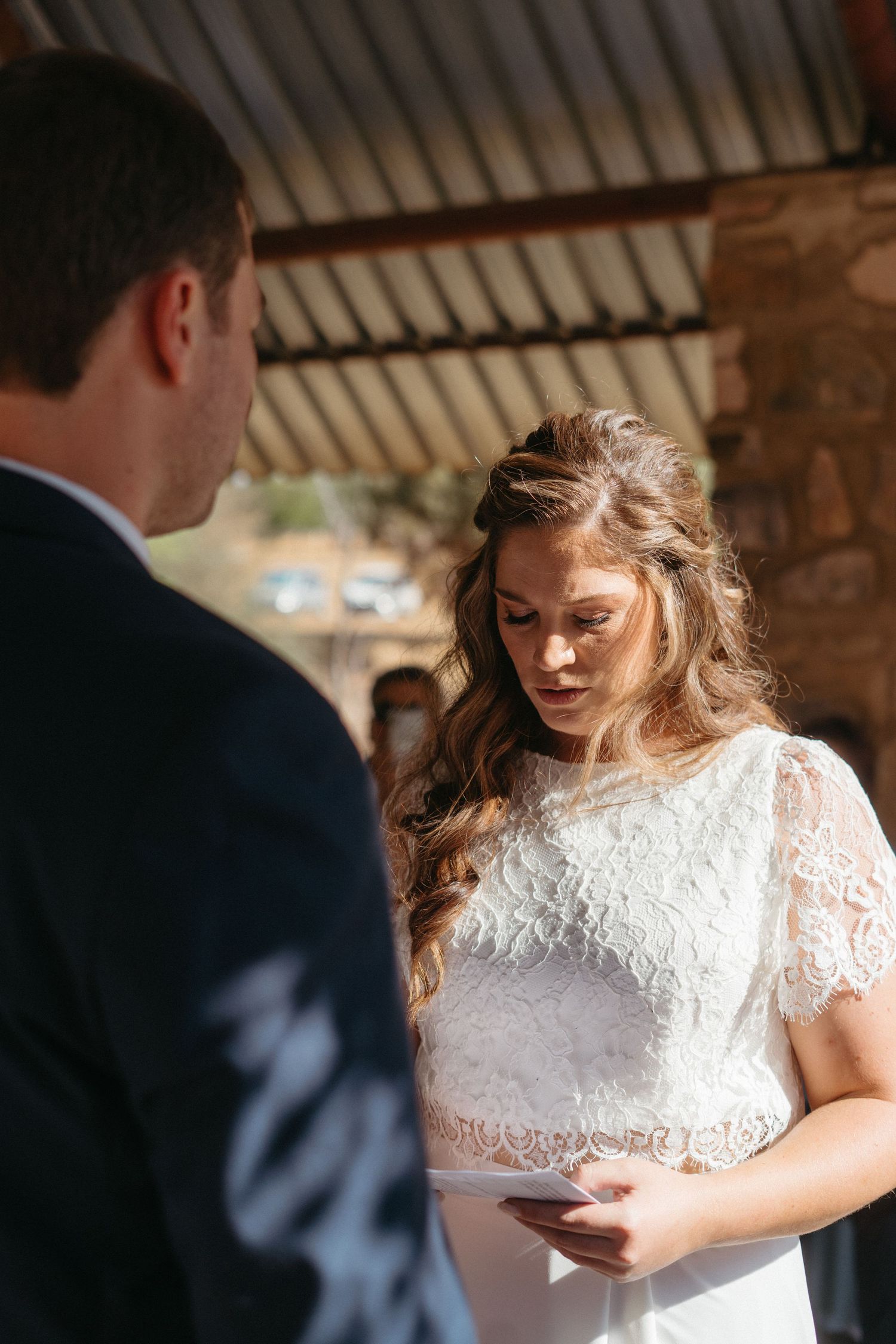 Wedding couple exchanging vows under a rustic wooden pavilion in an intimate outdoor ceremony.