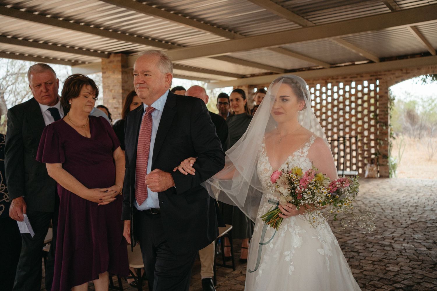 A traditional wedding ceremony processional moment captured under a rustic covered venue.