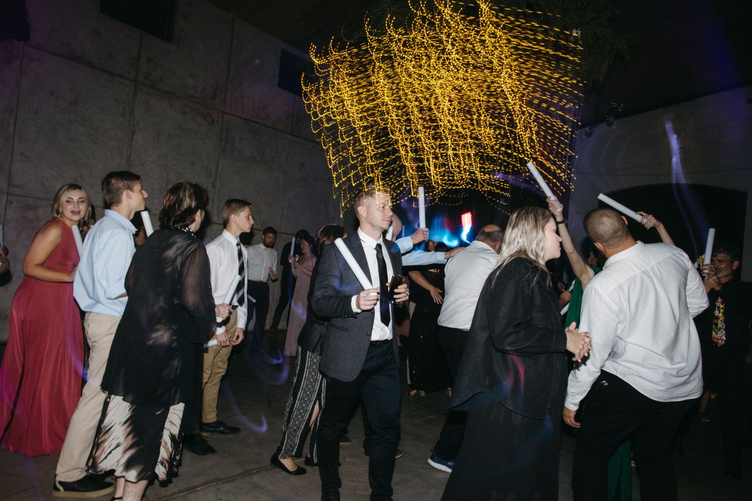 Party guests mingle beneath glowing yellow string lights at an evening event.