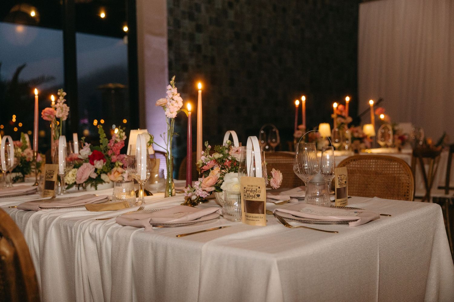 Elegant wedding reception table with candles, floral centerpieces, gold accents, and white linens in a romantic setting.