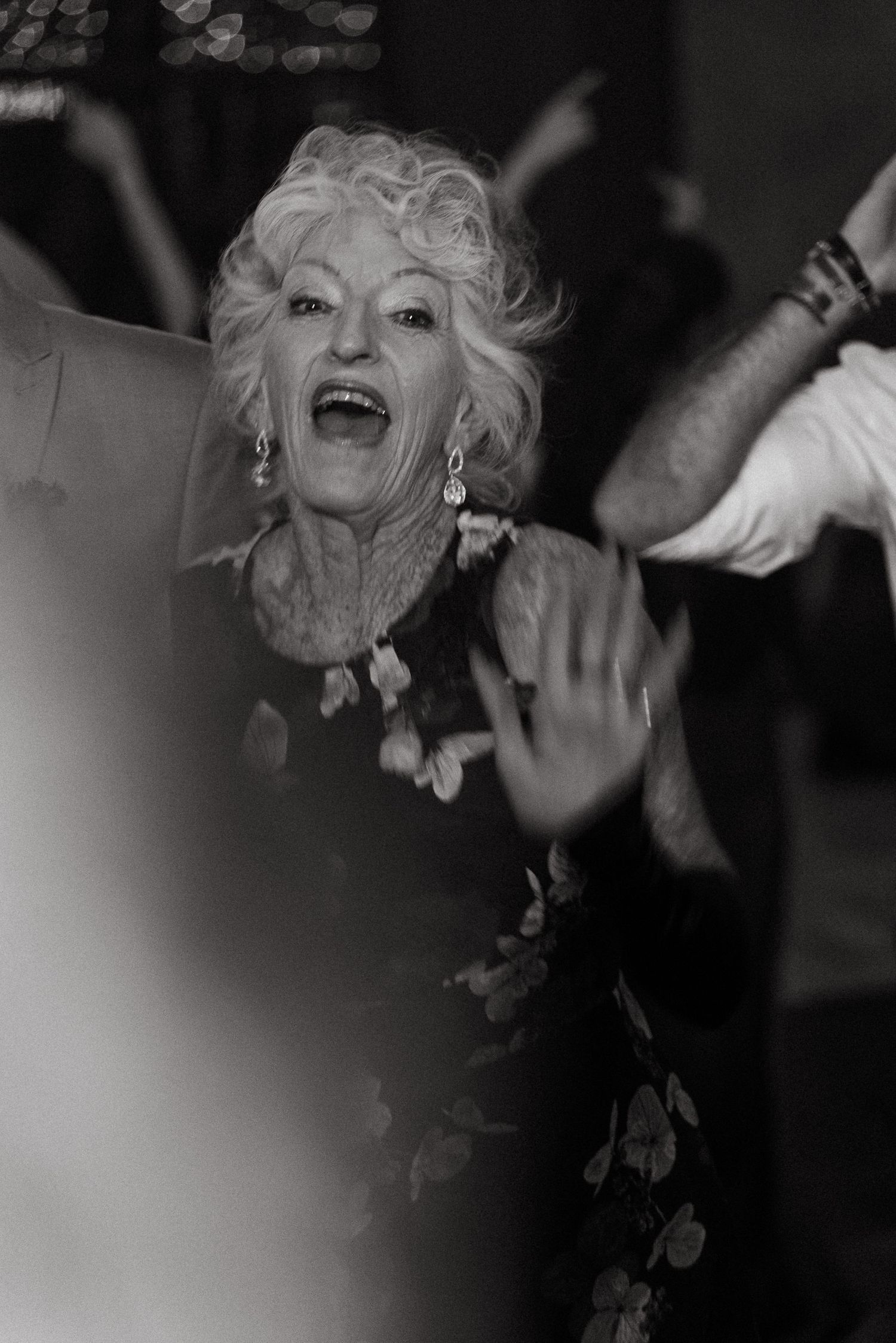 Elderly woman dancing joyfully at a celebration, captured in black and white photography.