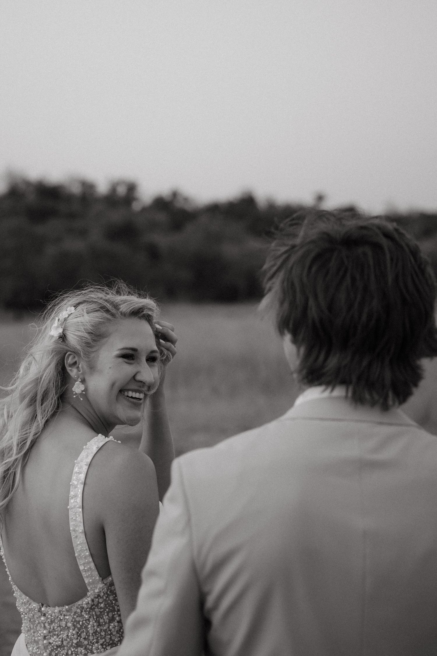 A joyful candid moment between a couple in formal attire standing in an outdoor field at dusk.