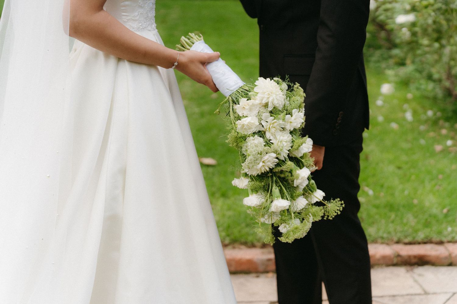 A romantic wedding photoshoot in a lush garden setting with elegant white florals and formal attire.
