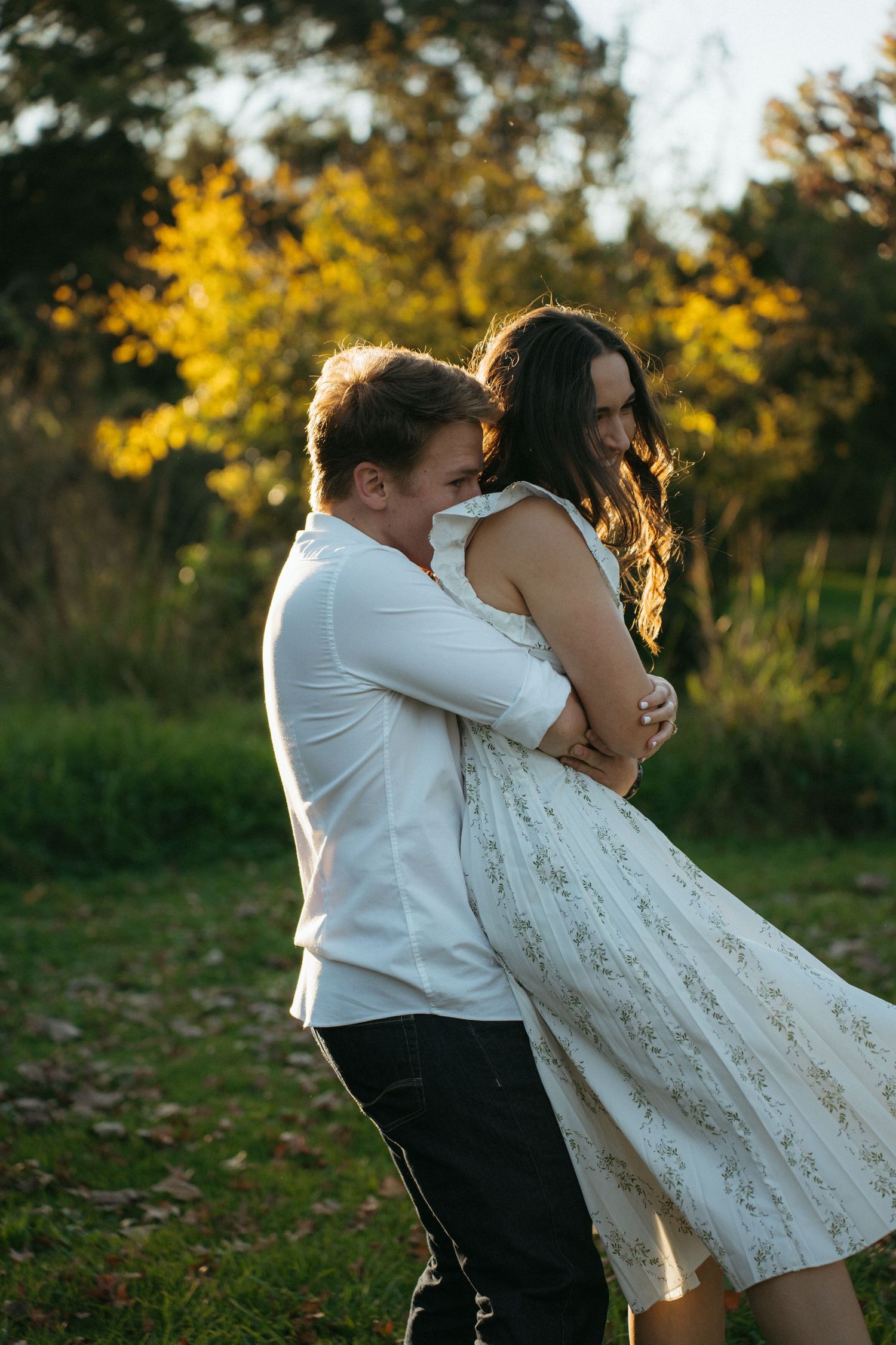 Romantic couple embraces in a sunlit autumn garden, her white lace dress flowing in the golden evening light.
