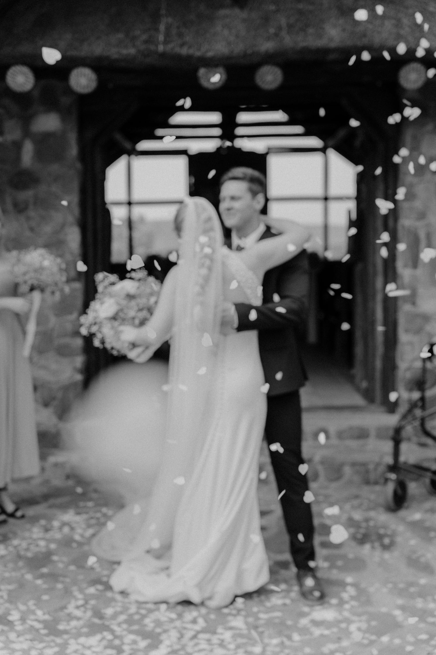 Wedding couple dancing with flower petals falling around them in black and white.