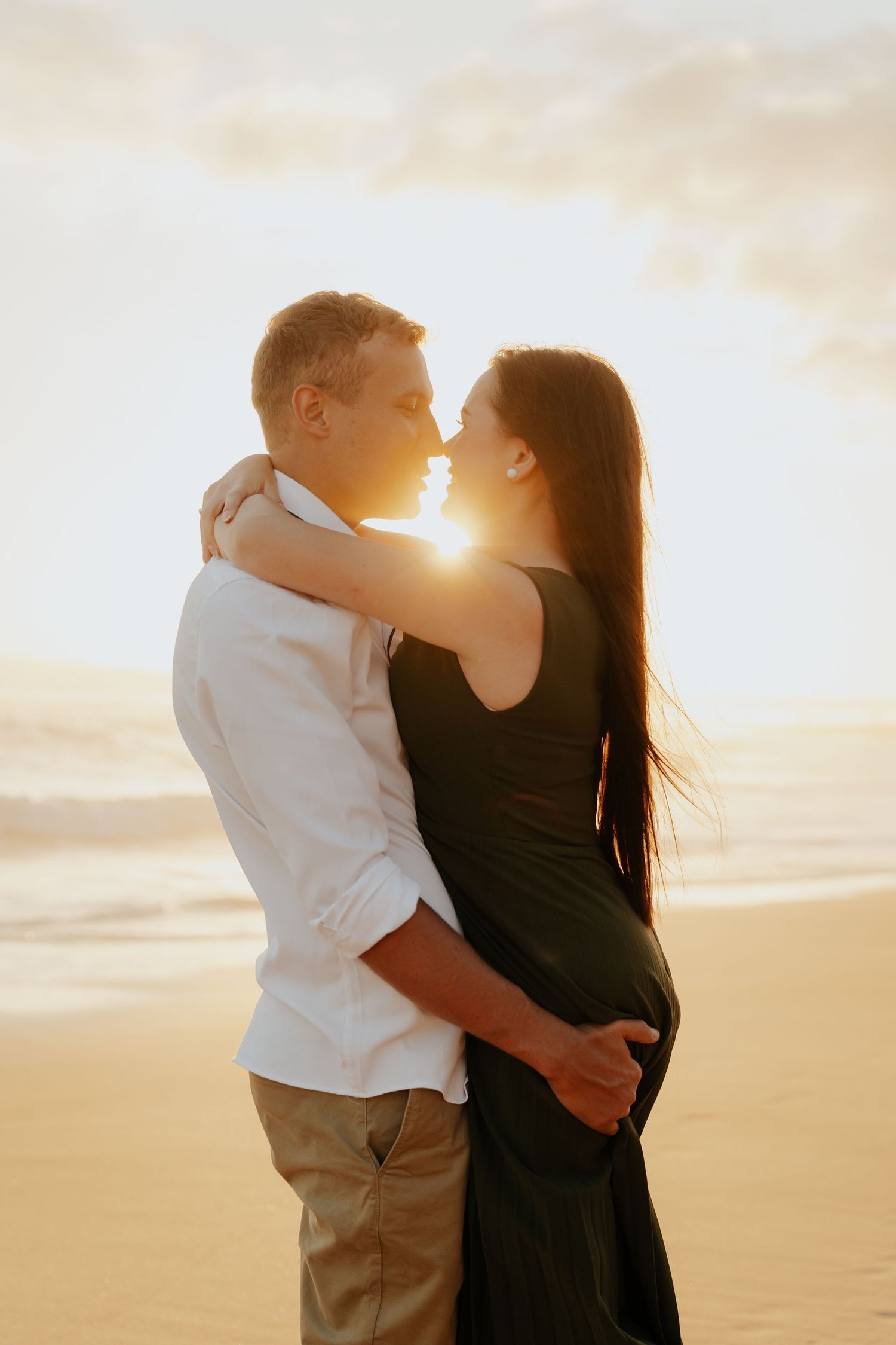 A romantic couple embraces on a sandy beach at sunset with golden sunlight streaming behind them in Western Cape