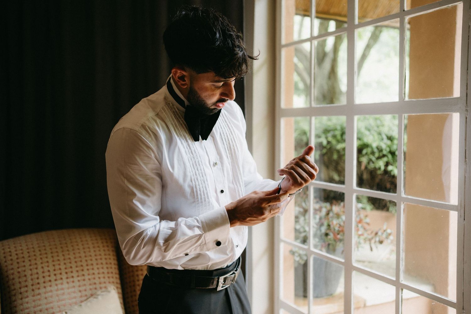 Person in formal white shirt checks phone while standing by window.