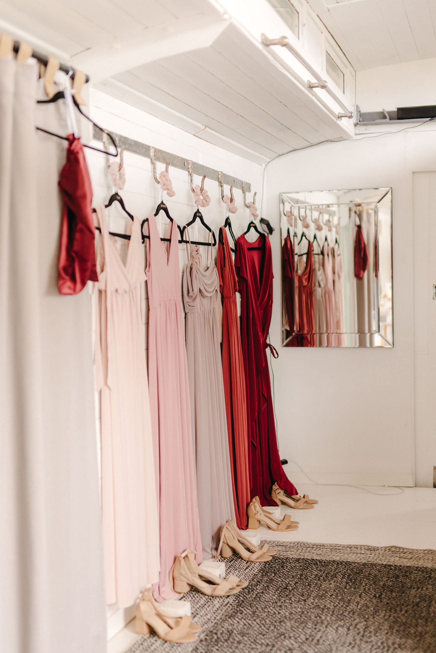 Elegant bridesmaid dresses in pink and red tones hang on a rack with matching shoes lined up underneath.