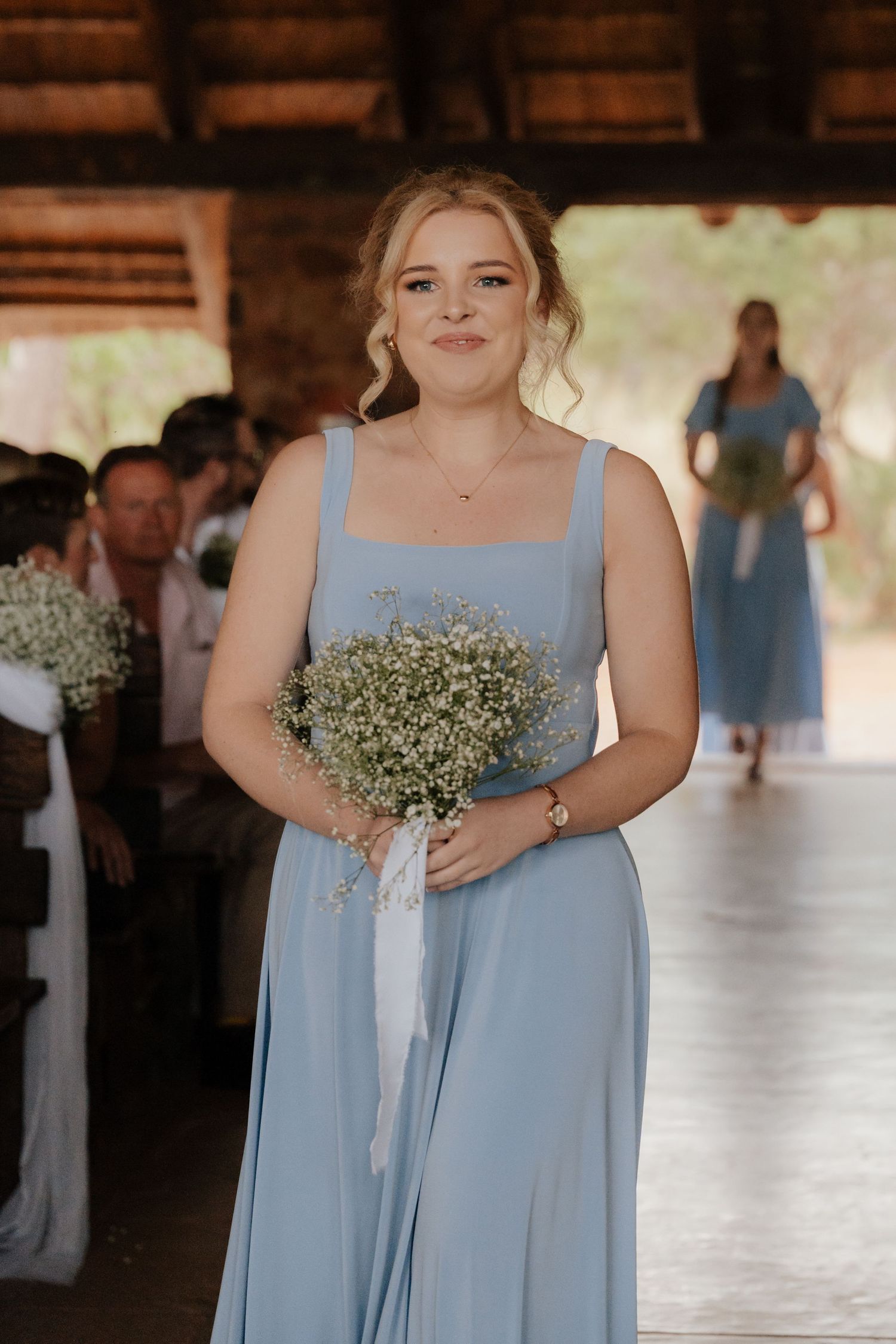 Bridesmaids in light blue dresses holding baby's breath bouquets at rustic venue.