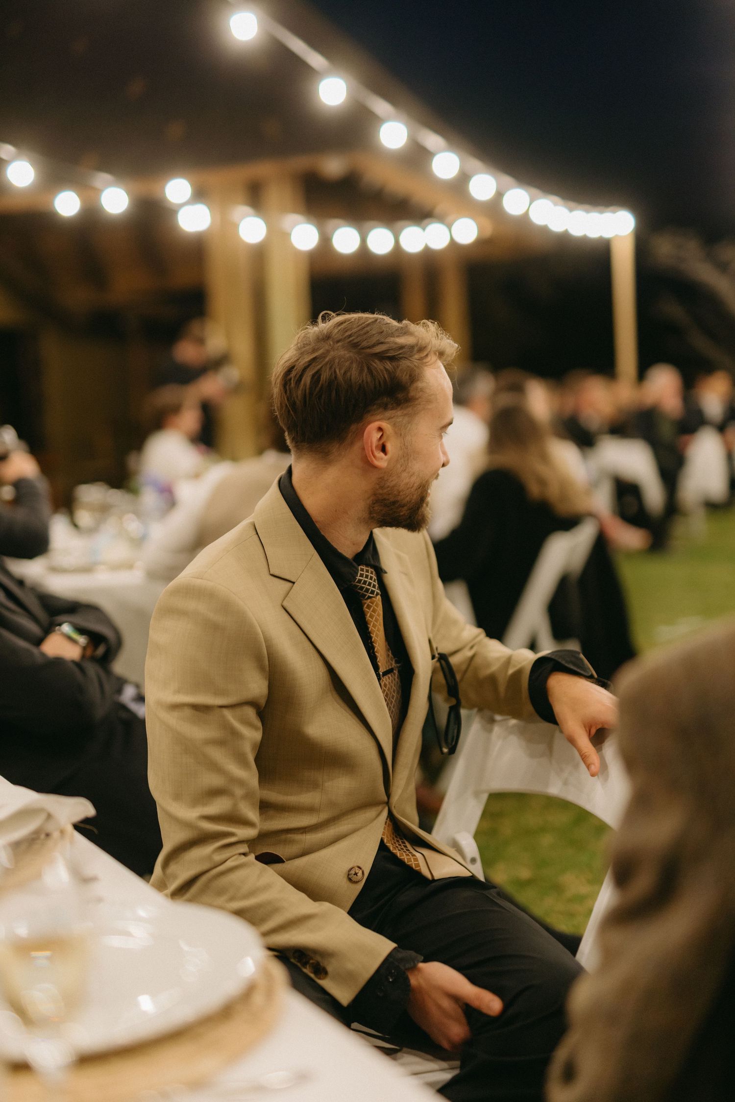 Evening wedding reception with string lights illuminating tables and guests under the night sky.