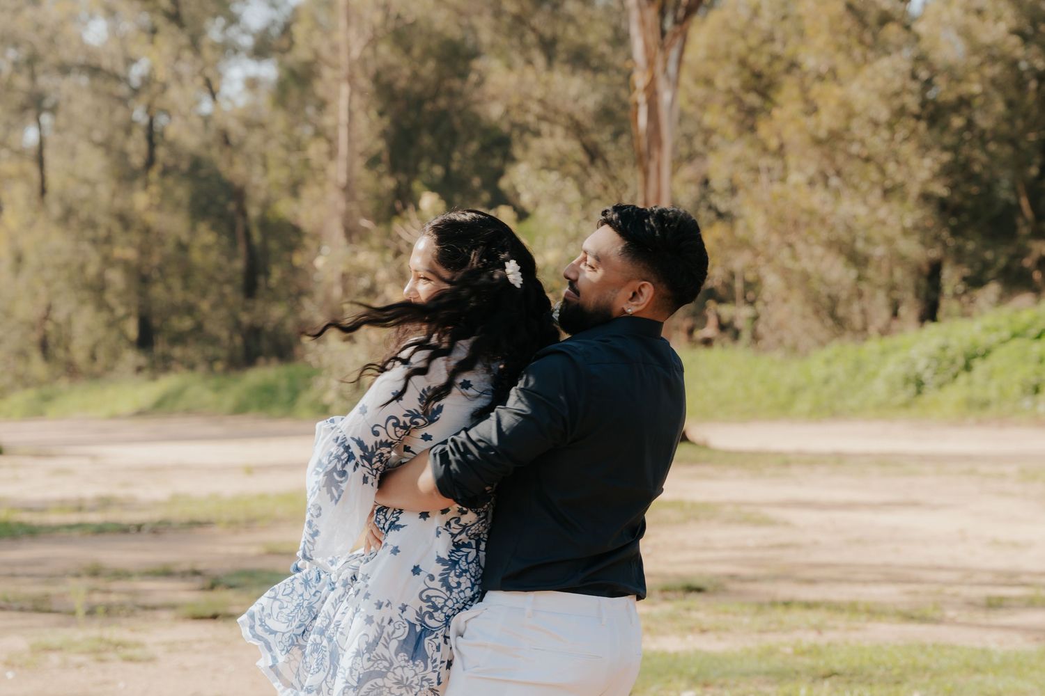 A couple shares a romantic moment in a sun-drenched field with golden light filtering through trees in the background.