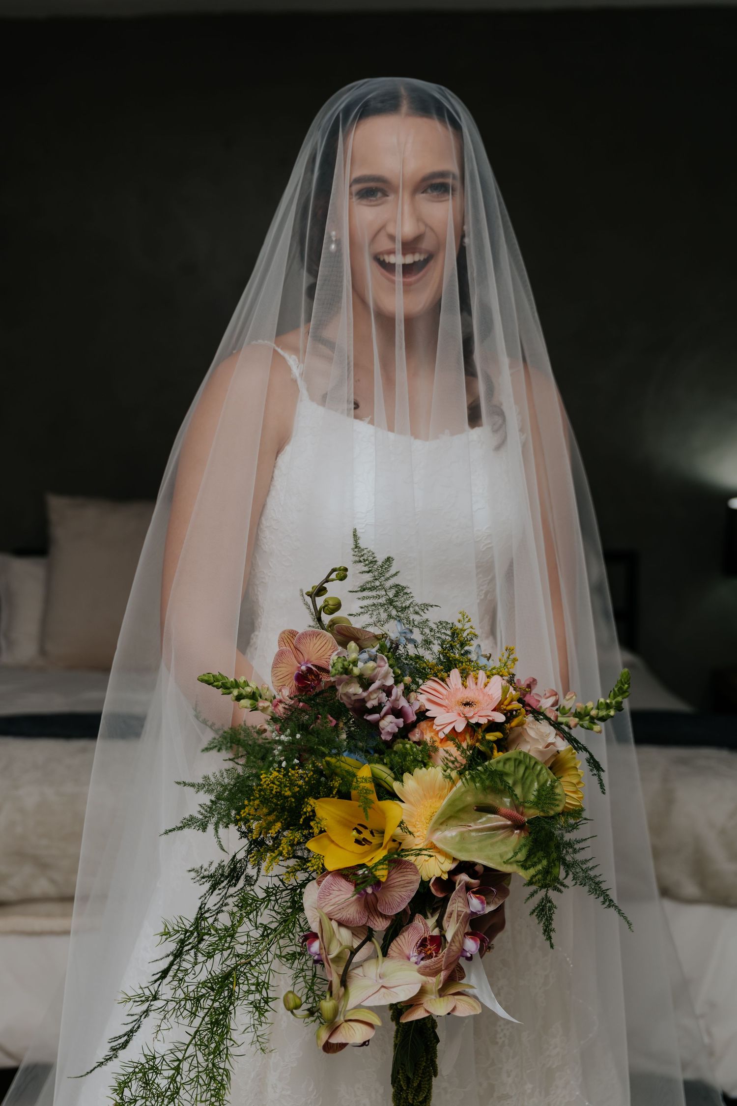 A bride in a white wedding dress holds a vibrant bouquet of yellow and pink flowers with cascading greenery.