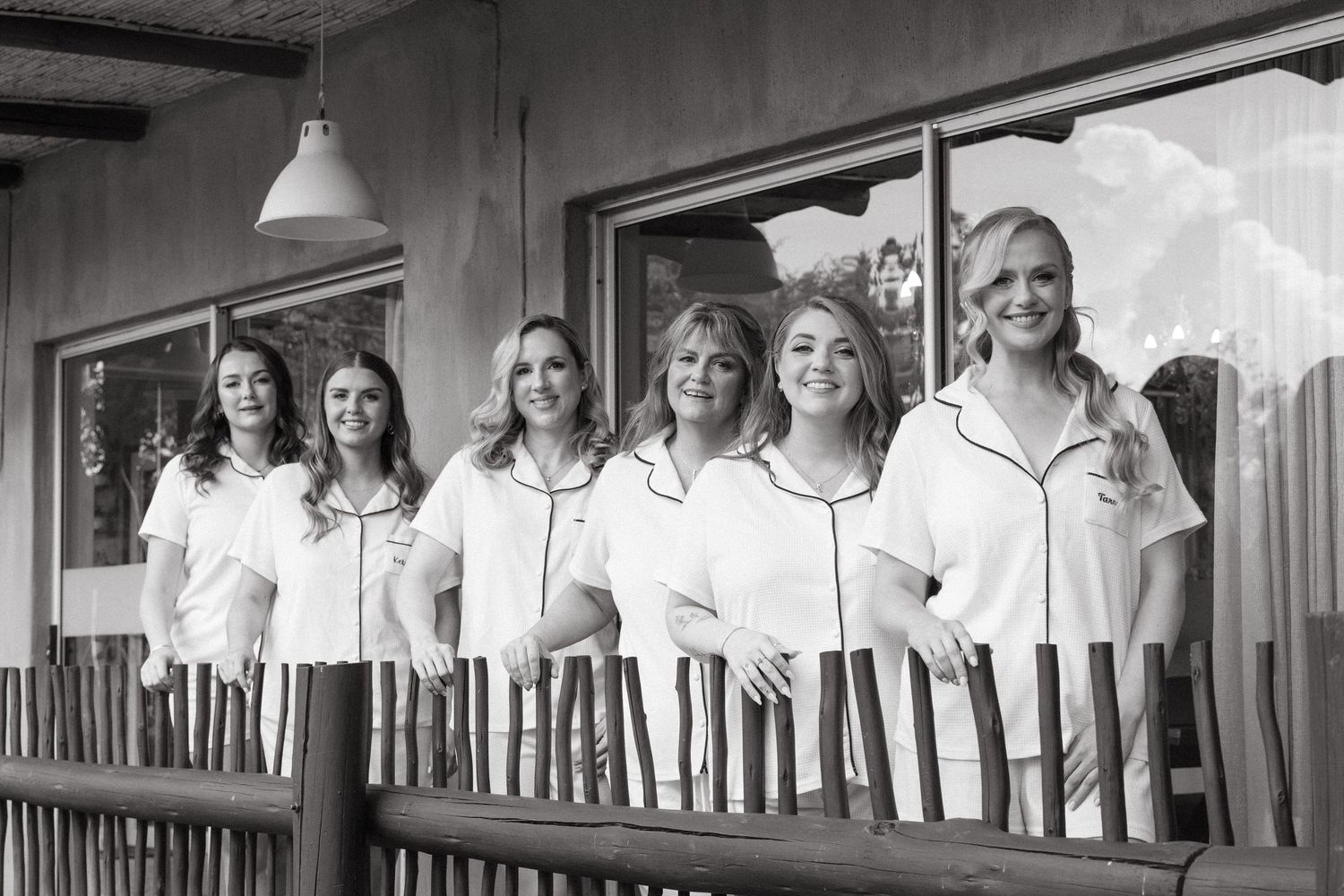 Black and white photo of bridesmaids in white dresses lined up in a row for a group portrait.