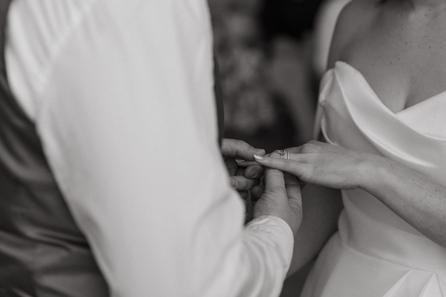 A close-up black and white shot of an engagement ring being placed on a finger during a wedding ceremony.