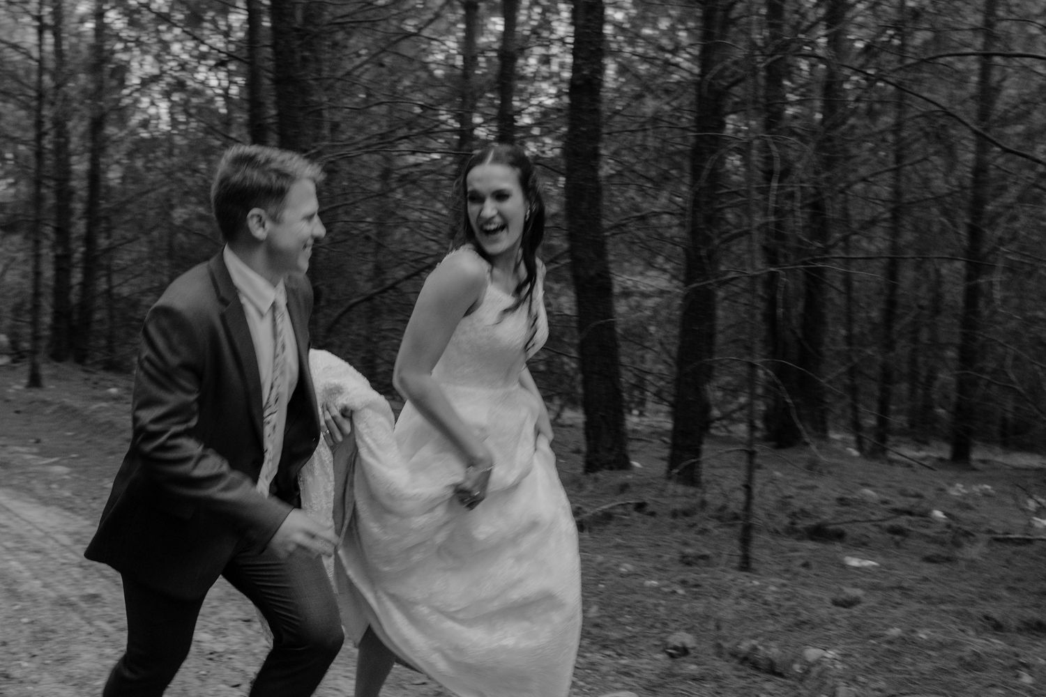 Bride and groom laughing while running through a forest near Lydenburg, Mpumalanga in black and white wedding photo.