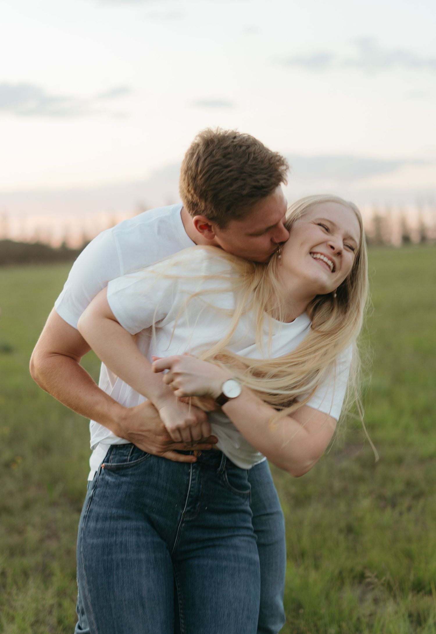 Romantic moment captured between couple in white shirts and jeans at sunset in a field.