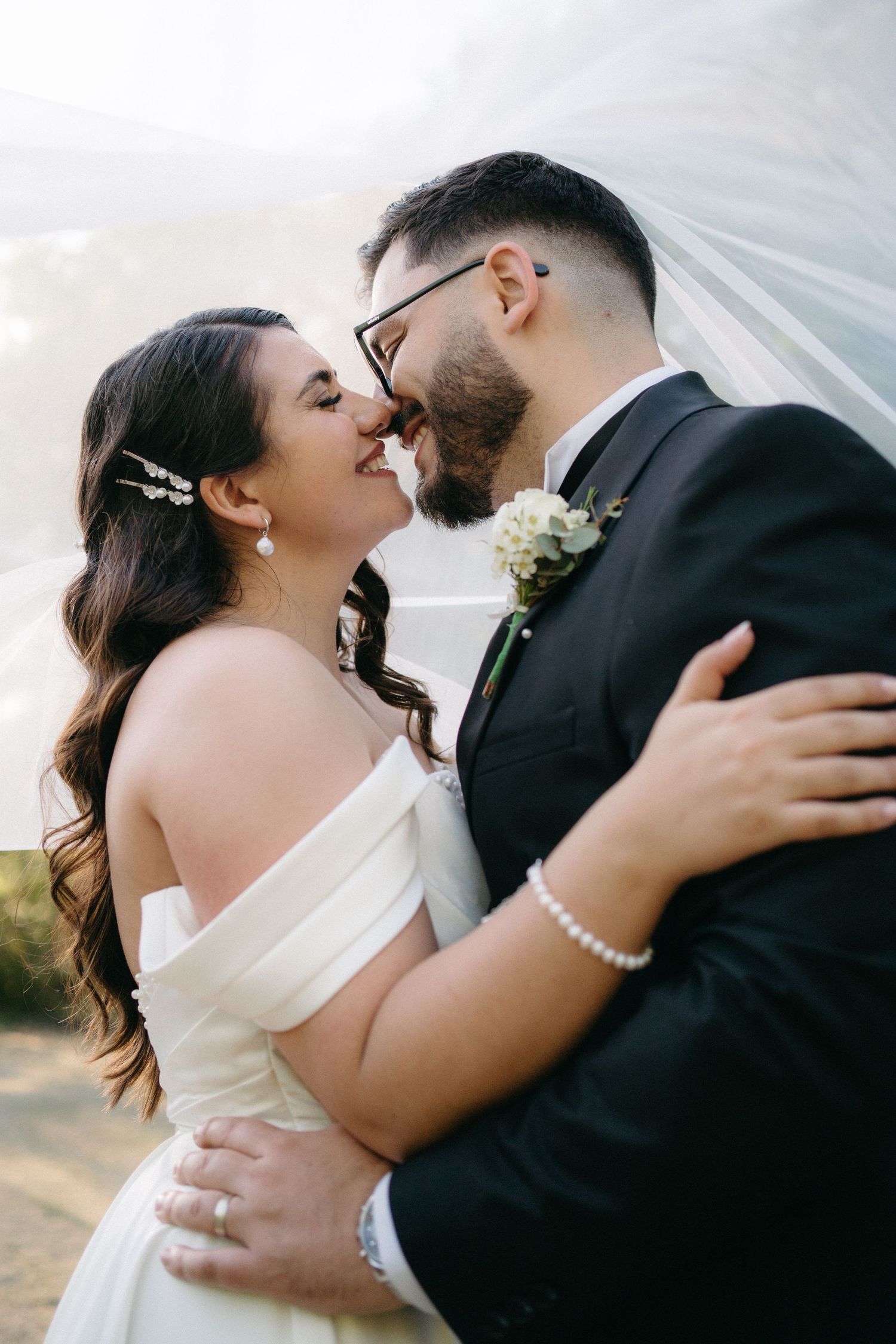 A romantic wedding moment captured as newlyweds share an intimate embrace under billowing veil outdoors.