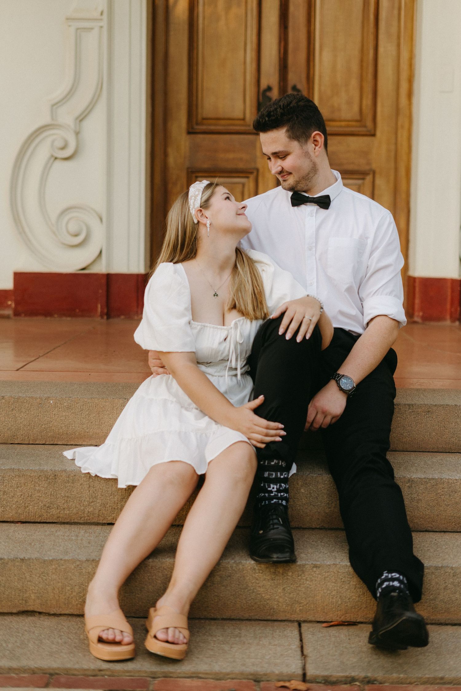 A couple shares an intimate moment while sitting on stone steps in front of a wooden door.