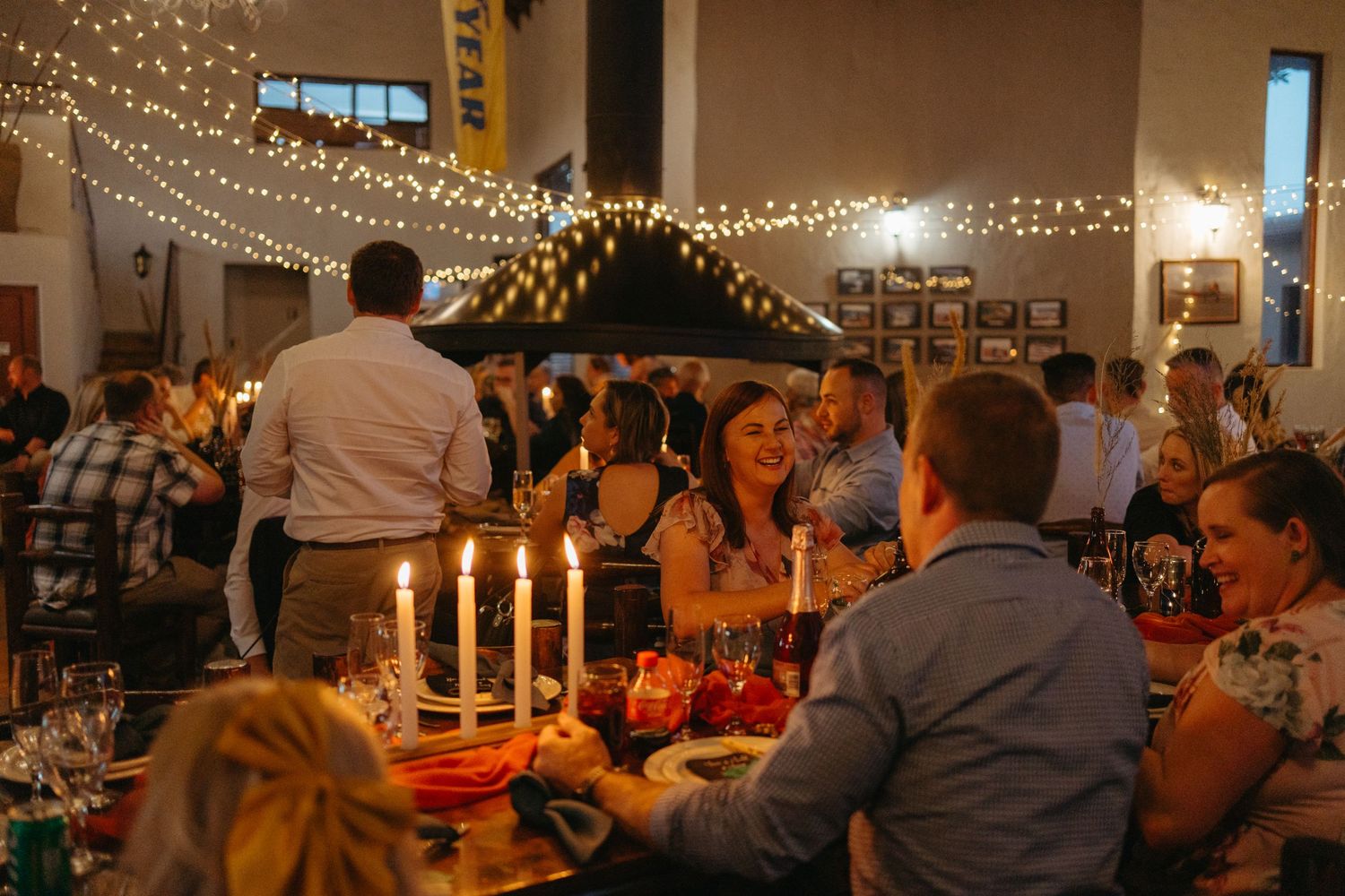 Wedding reception dinner table set with candles and string lights creating a warm ambiance.