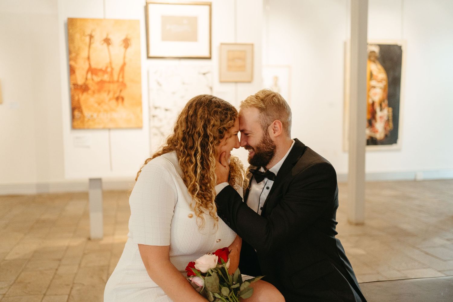 Intimate moment shared between couple in formal attire at an art gallery.
