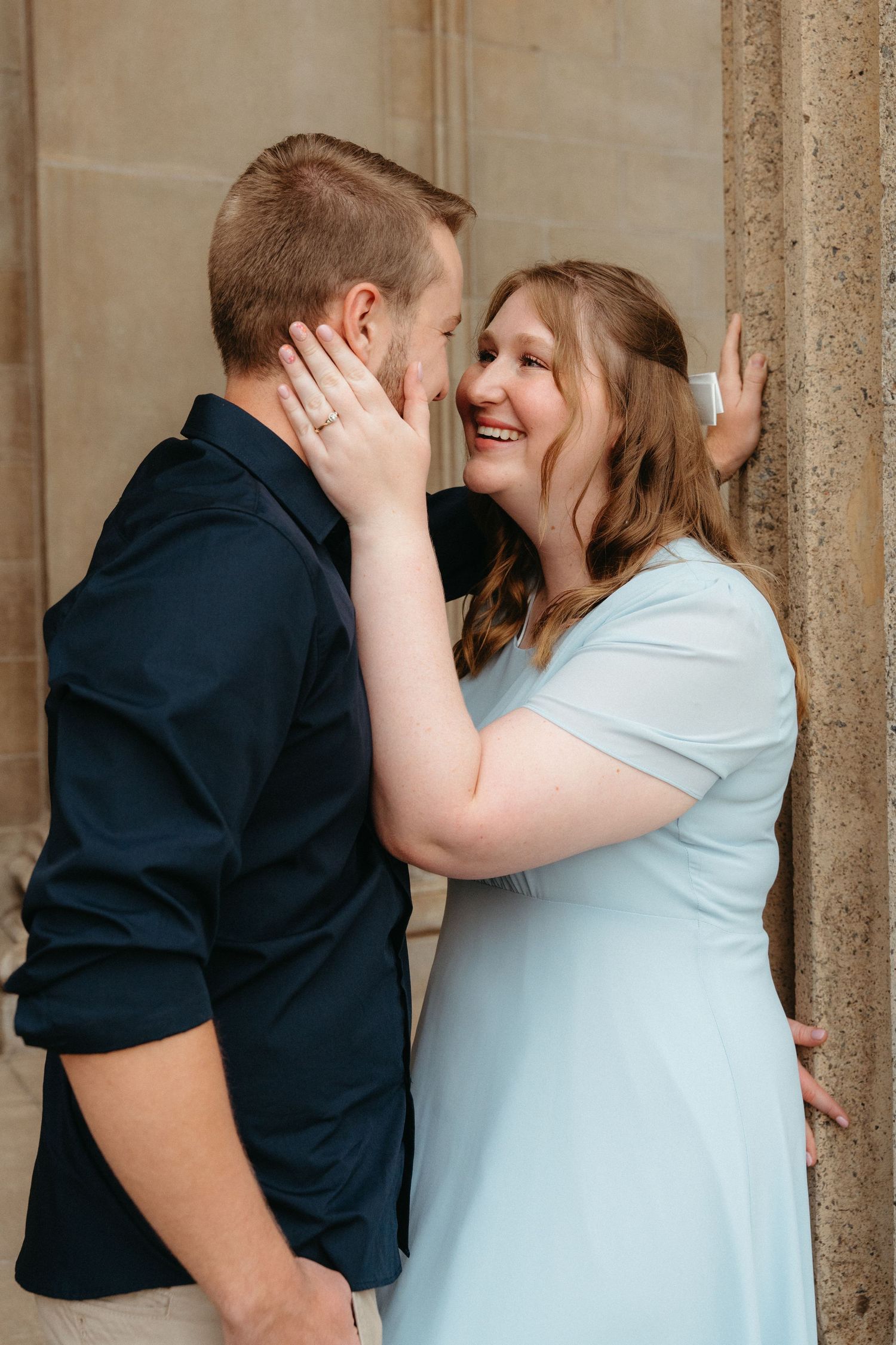 A romantic couple in navy and white outfits share intimate moments against stone columns in a photo series.