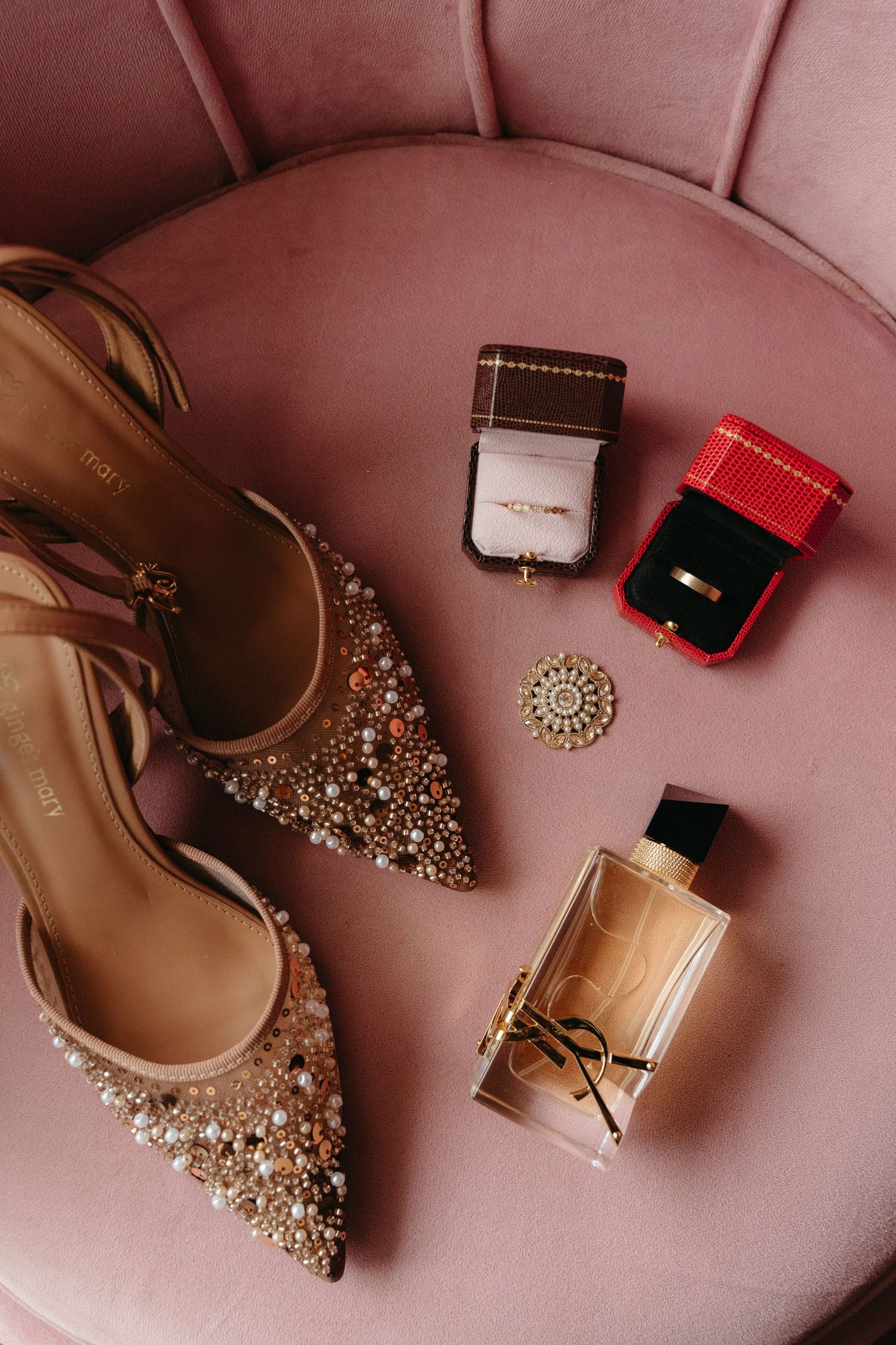 Sparkly gold heels, perfume bottle, and jewelry boxes arranged on pink velvet surface for wedding day details.