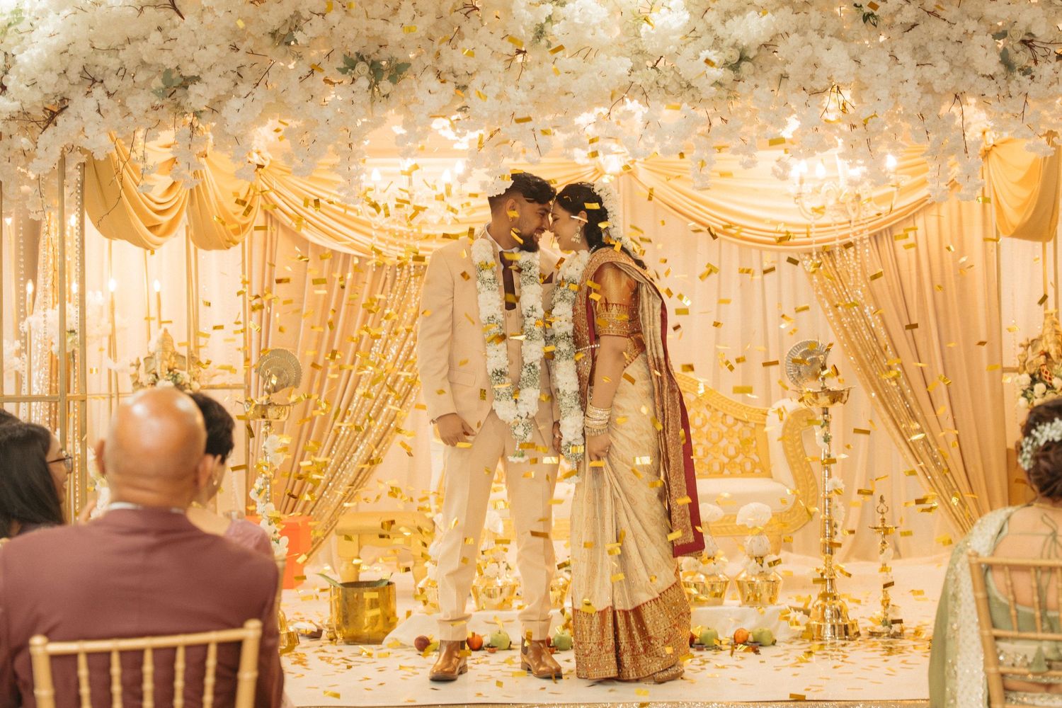 Elegant wedding reception venue decorated with ornate chandeliers, floral arrangements, and white drapery creating a luxurious atmosphere.