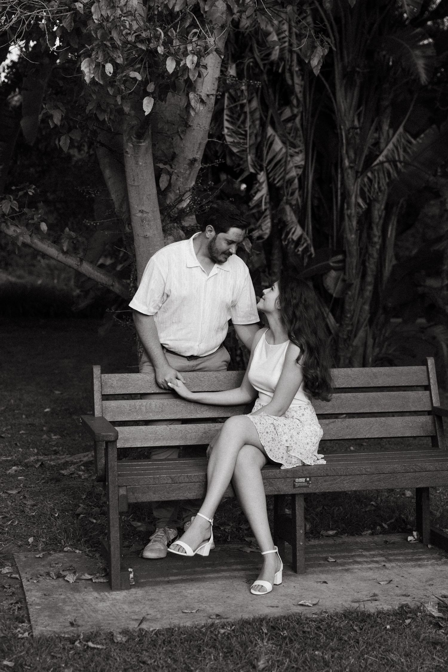 Black and white photo of a couple sitting on a park bench, smiling and gazing at each other.