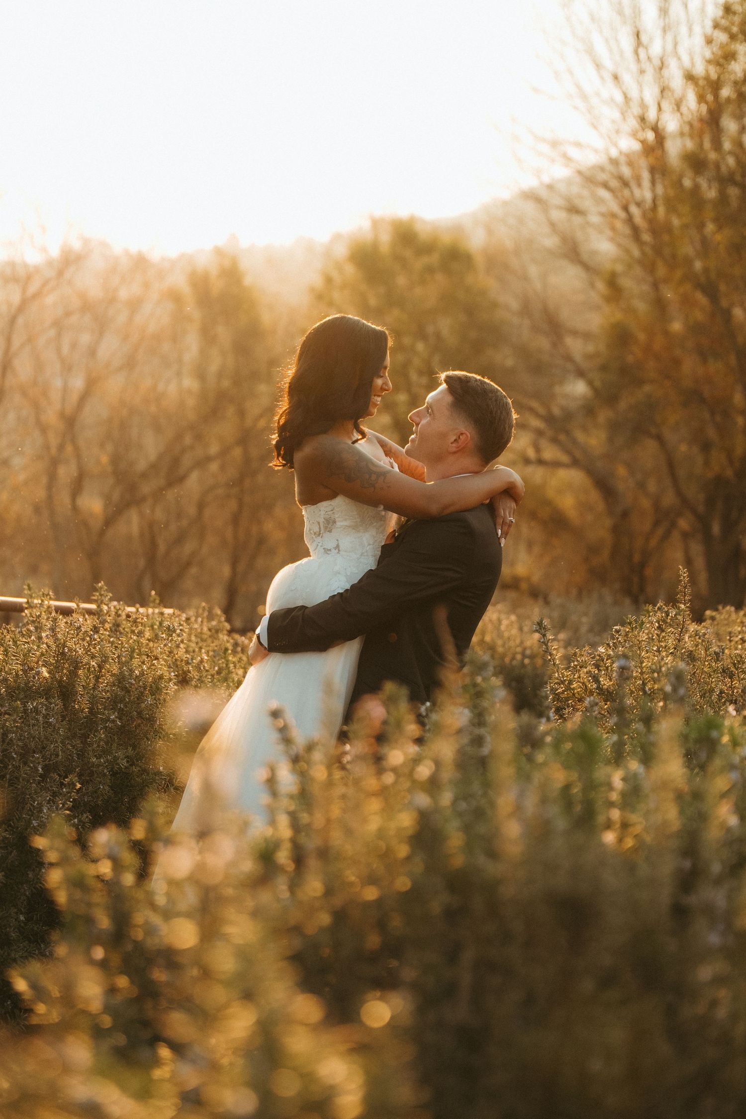 A bride and groom embrace in a golden sunlit field in Muldersdrift during their outdoor wedding ceremony at sunset.
