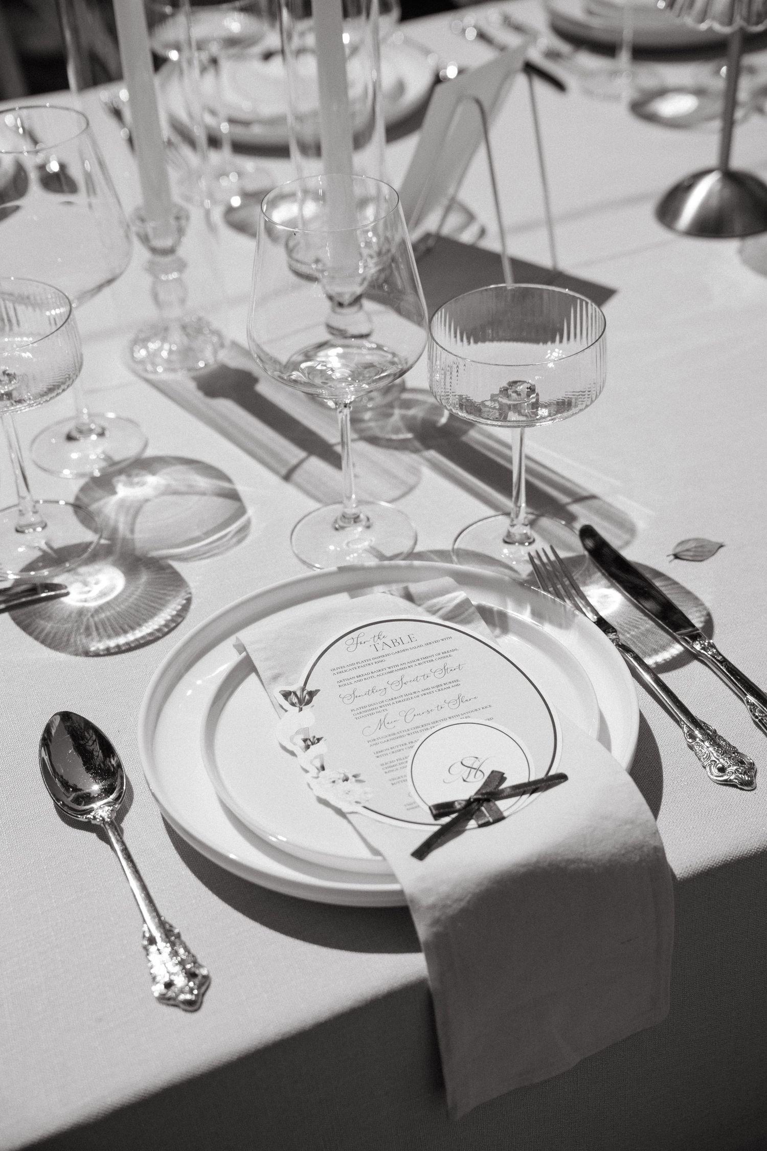 Elegant black and white formal place setting with crystal glasses, silver cutlery, white plate, and menu card on white tablecloth.