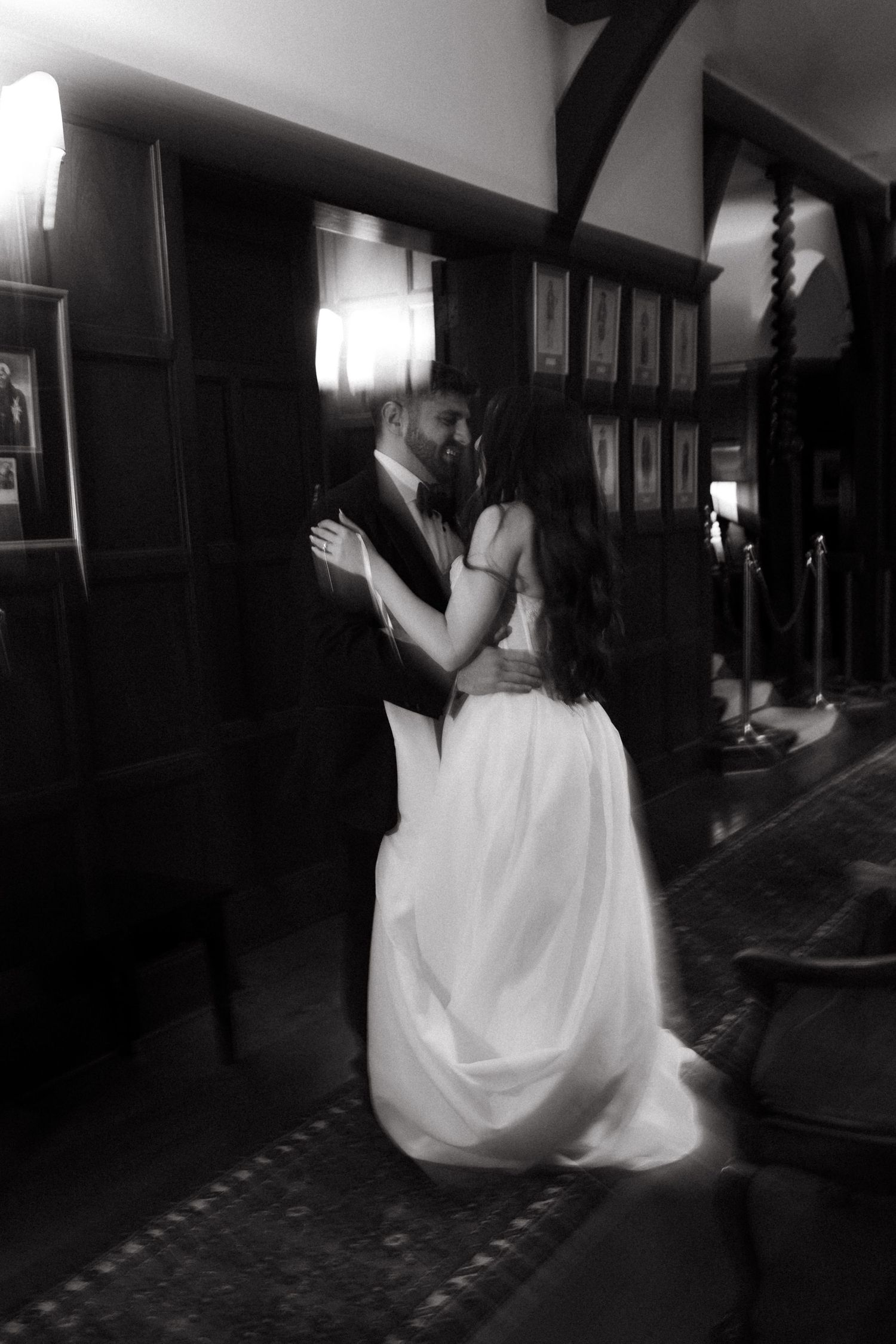 Black and white photo of a bride and groom sharing their first dance in an elegant wood-paneled ballroom.