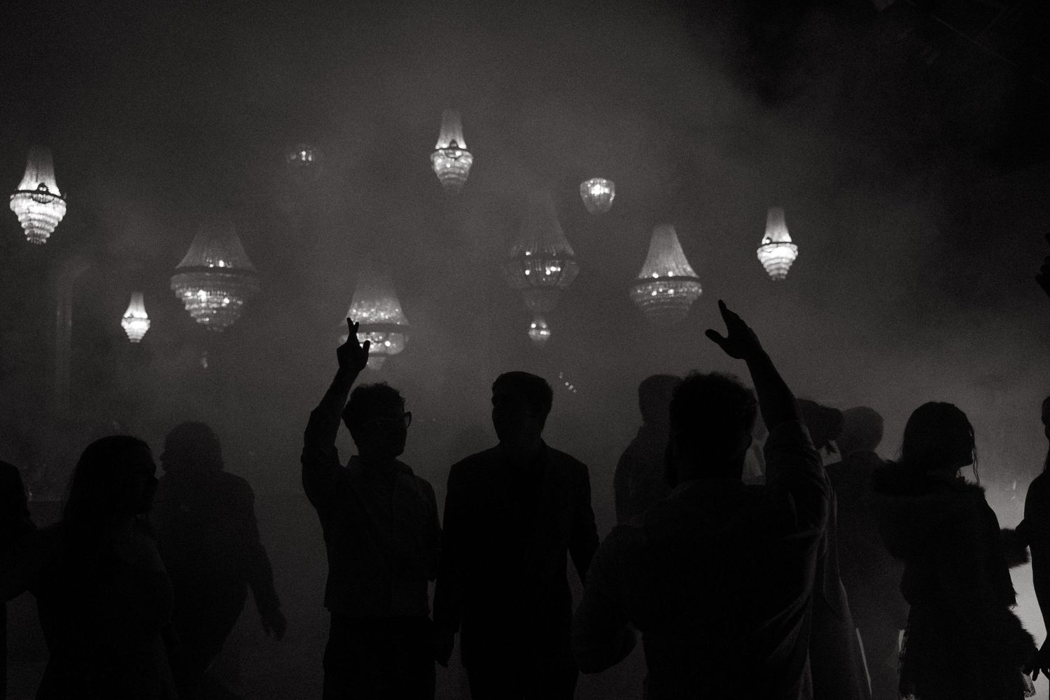 Silhouettes of people pointing at glowing lanterns in a misty night sky, black and white photography.