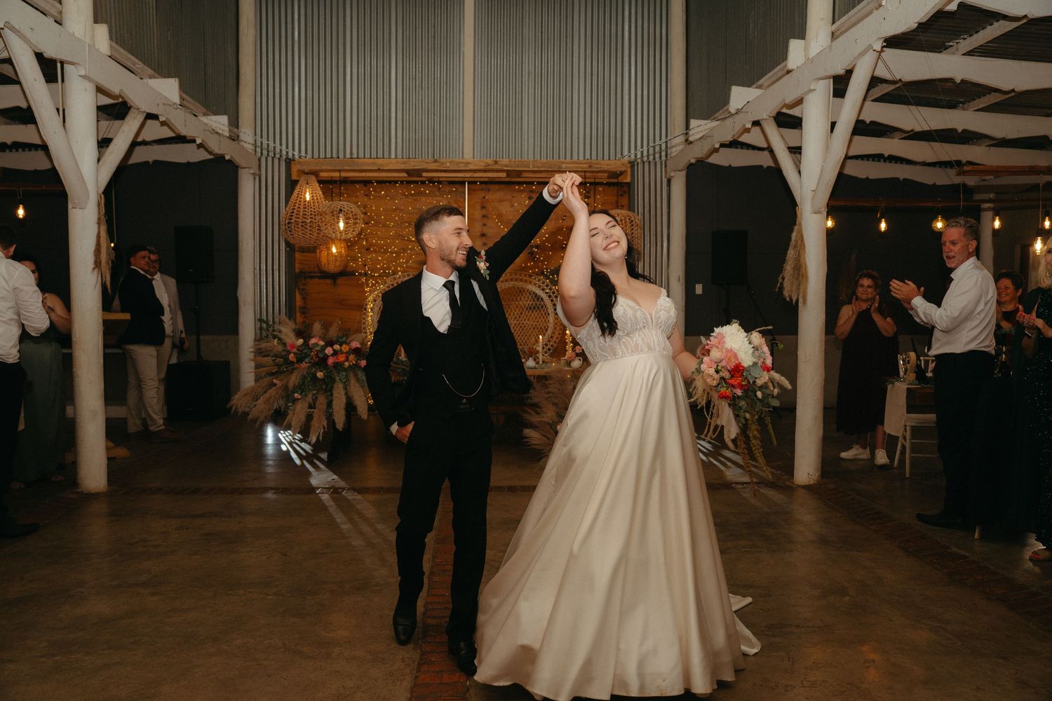 A couple shares their first dance in a rustic barn venue decorated with string lights.