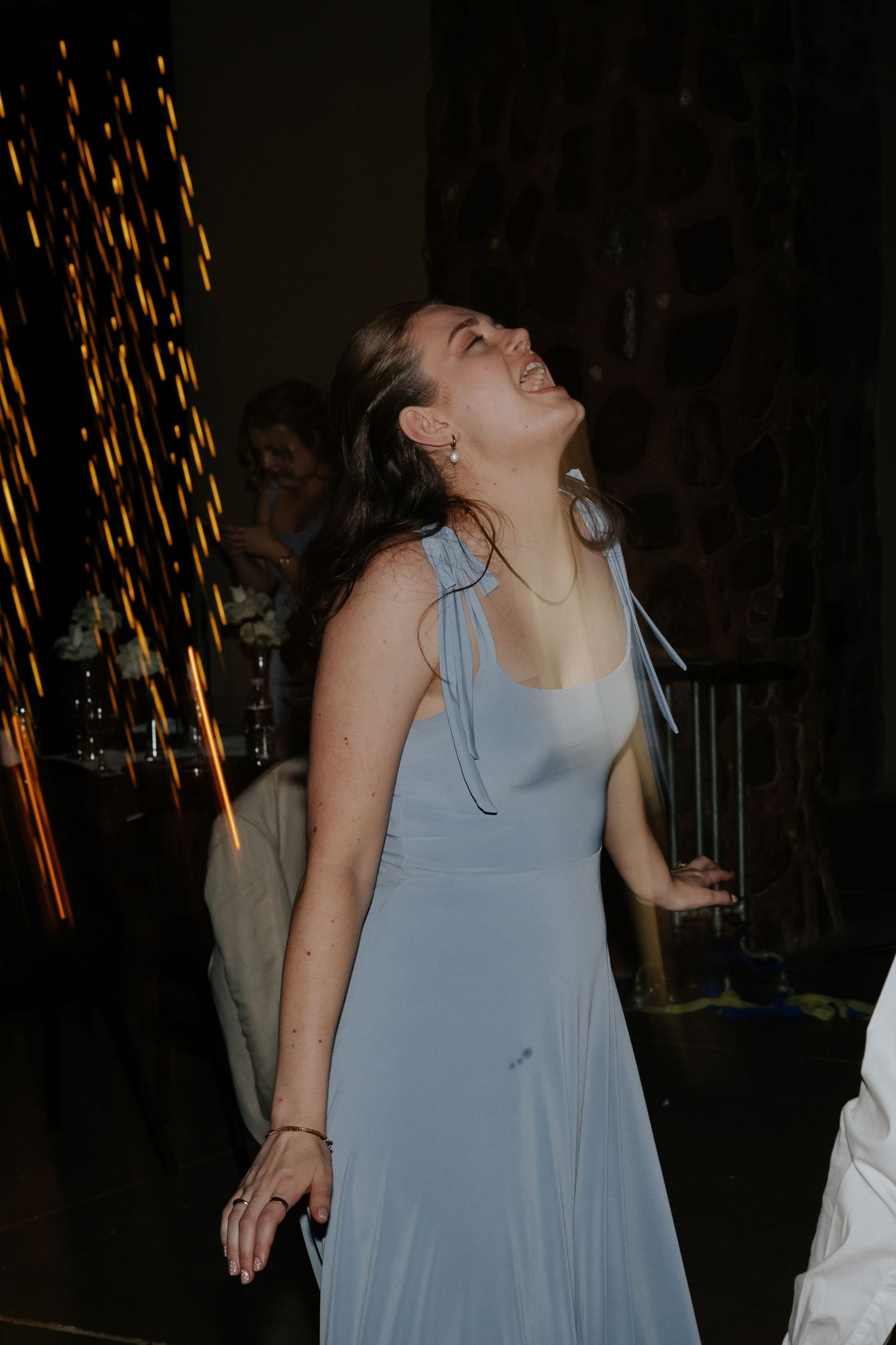 A person in a light blue dress dances joyfully under sparkler lights at a wedding reception.