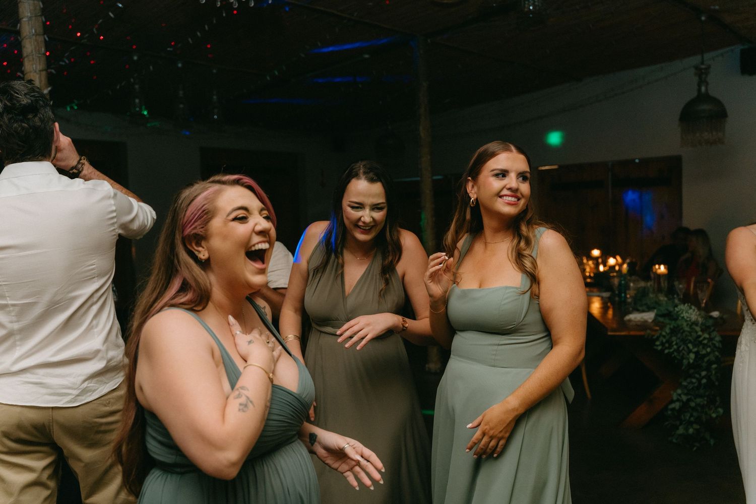 Wedding guests dance and celebrate on a dimly lit dance floor during an evening reception.