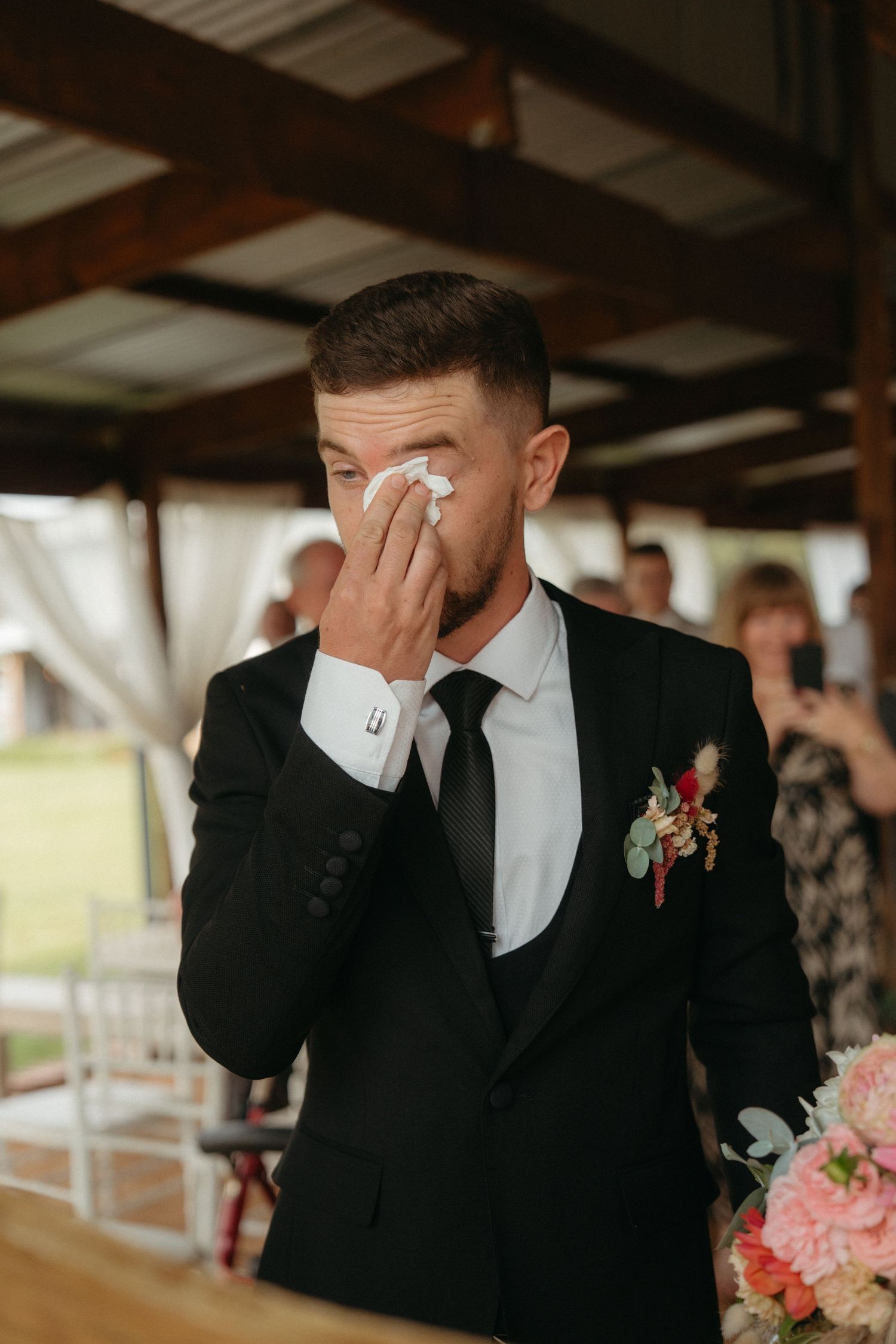 Emotional moment during wedding ceremony showing formal attire and pink floral boutonniere.