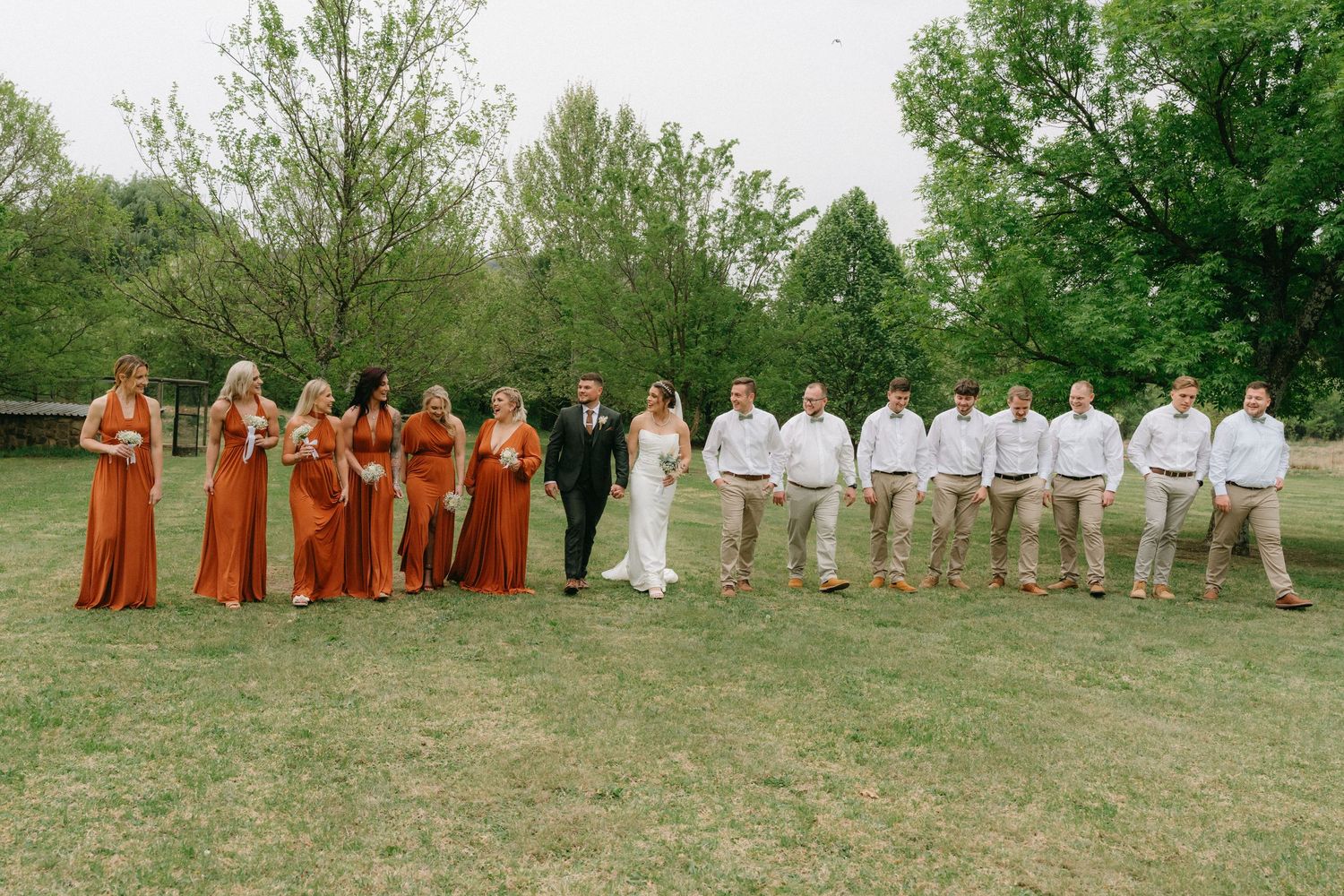 Wedding party in rust orange and white attire posing outdoors in a natural setting.